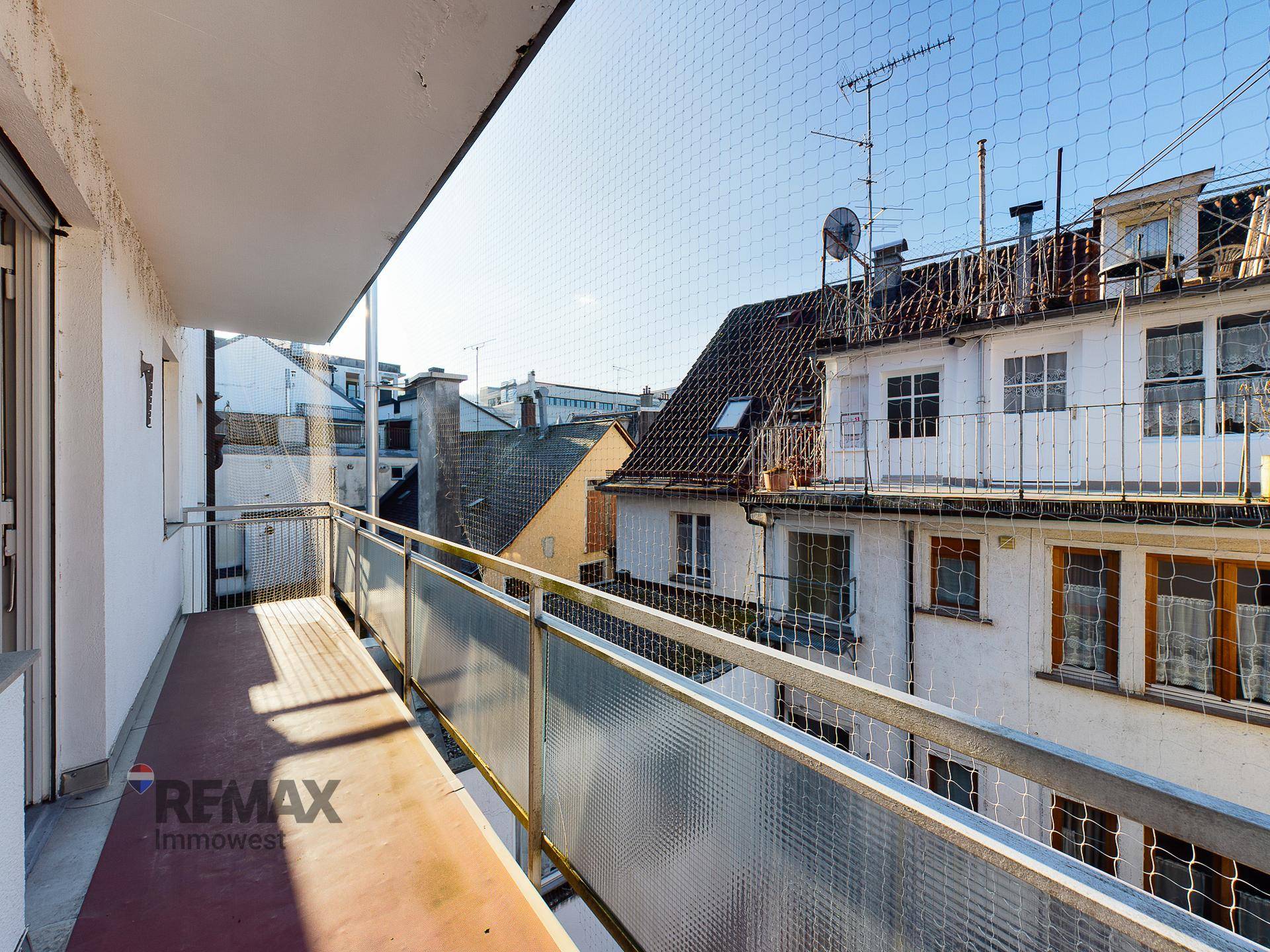 Langer Balkon mit Metallgeländer und Blick auf die Dächer der umliegenden Gebäude.