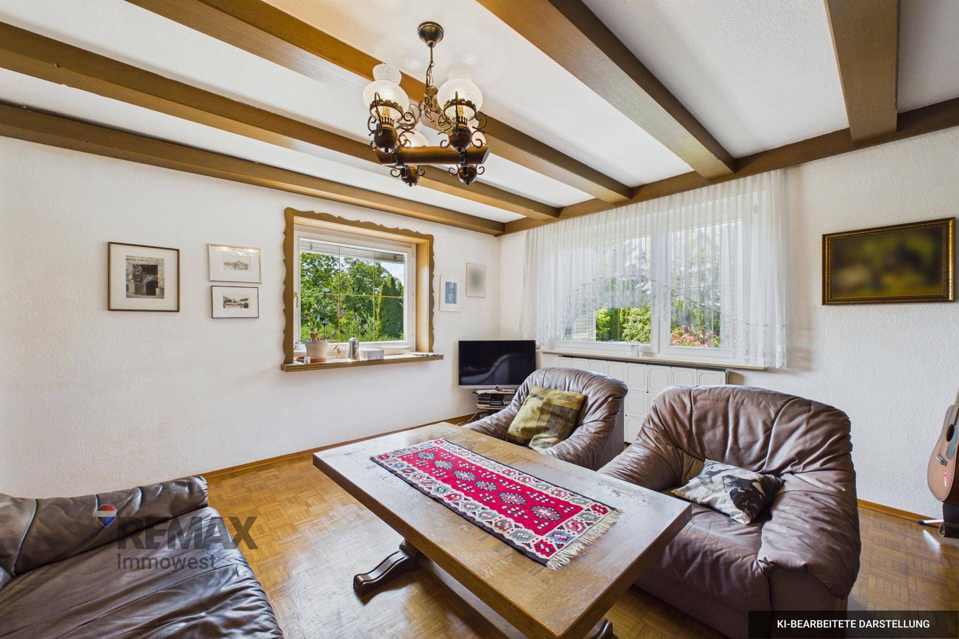 Gemütliches Wohnzimmer mit sichtbaren Holzbalken, Ledersofas und einem Holztisch, Blick ins Grüne.