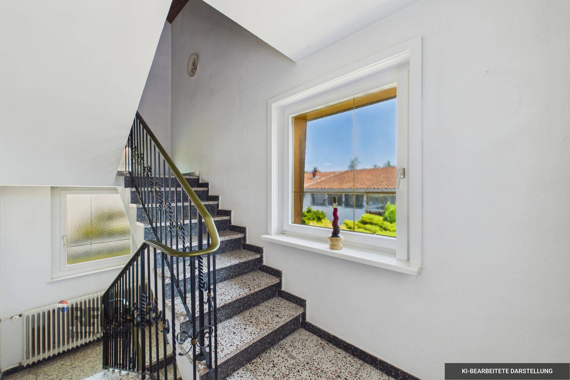 Treppenhaus mit Terrazzostufen und schmiedeeisernem Geländer, hell durch großes Fenster.