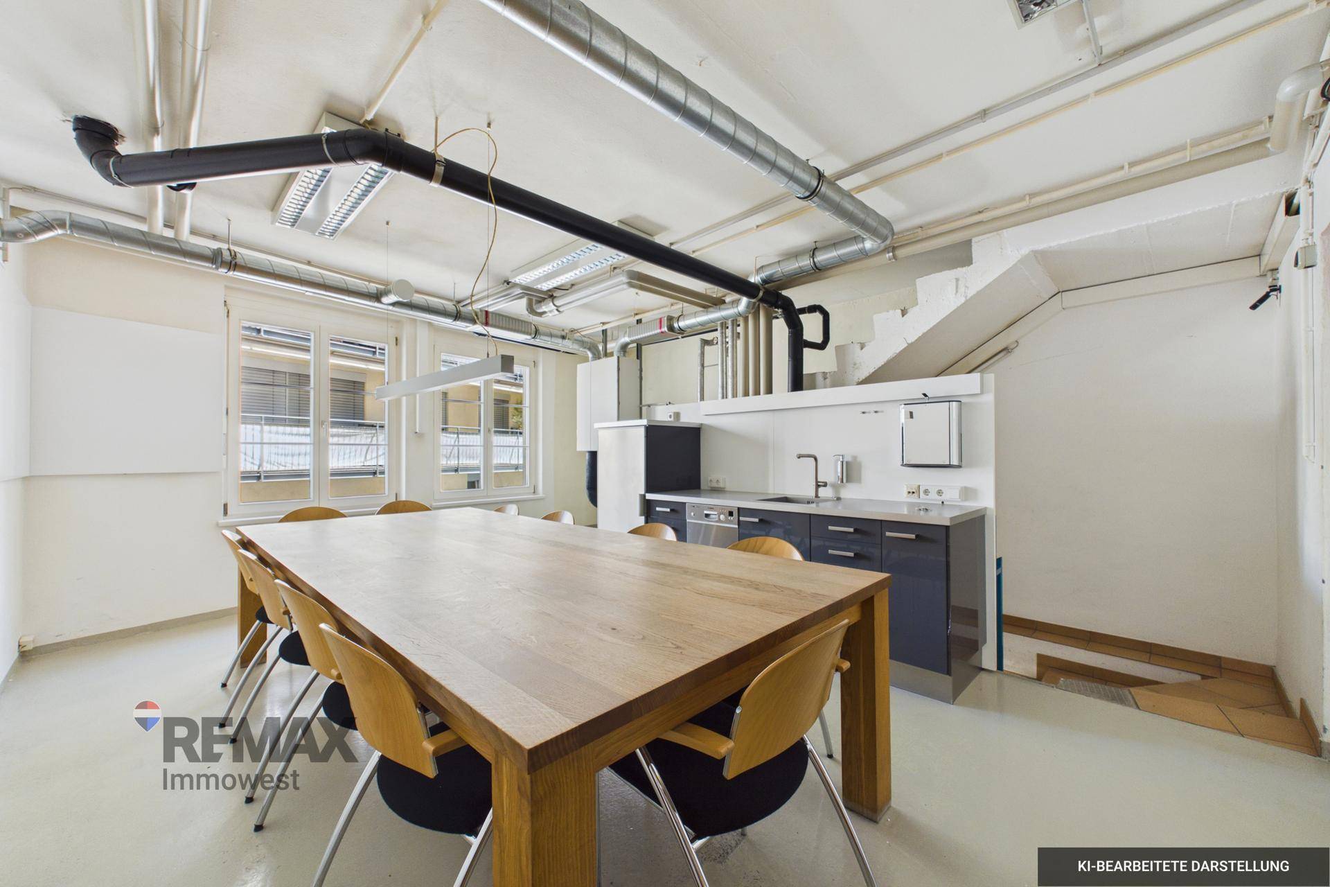 Geräumiger Büroraum mit integrierter Küchenzeile, Holztisch und sichtbaren Lüftungsrohren an der Decke.