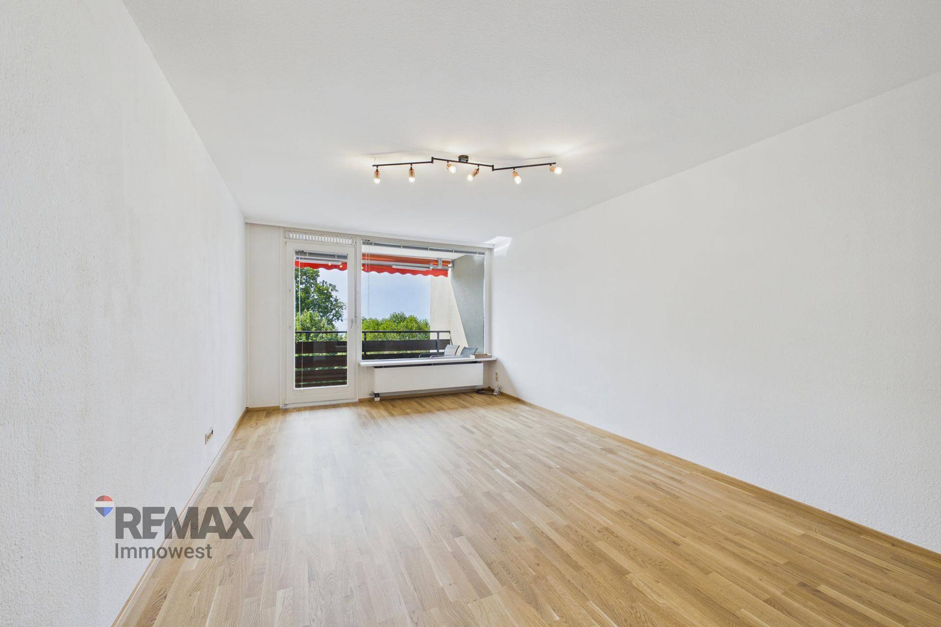 Heller Wohnraum mit Parkettboden und Zugang zu einem Balkon mit roter Markise.