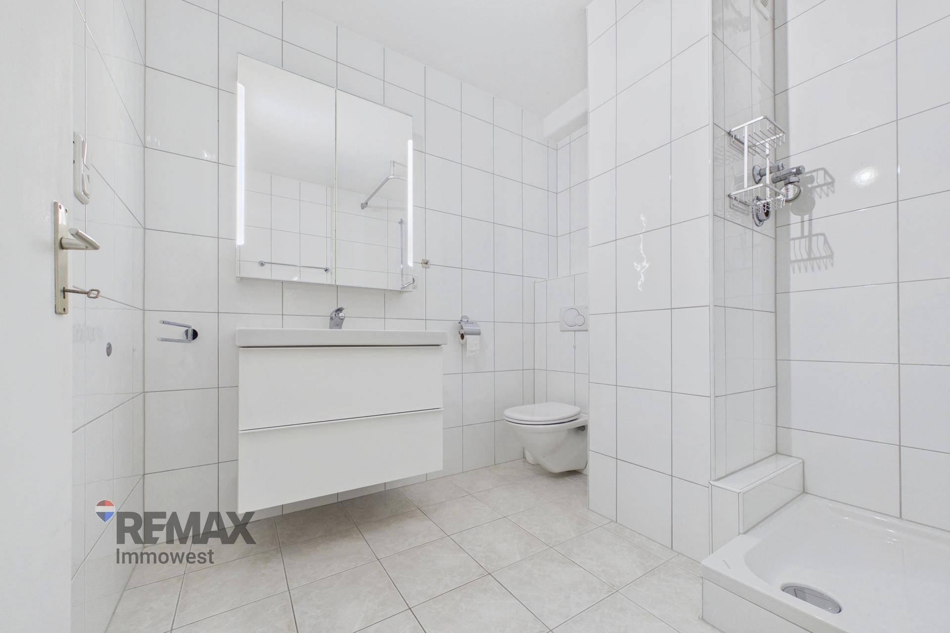 Modern gefliestes Badezimmer in Weiß mit Waschtisch, Spiegelschrank und Toilette.