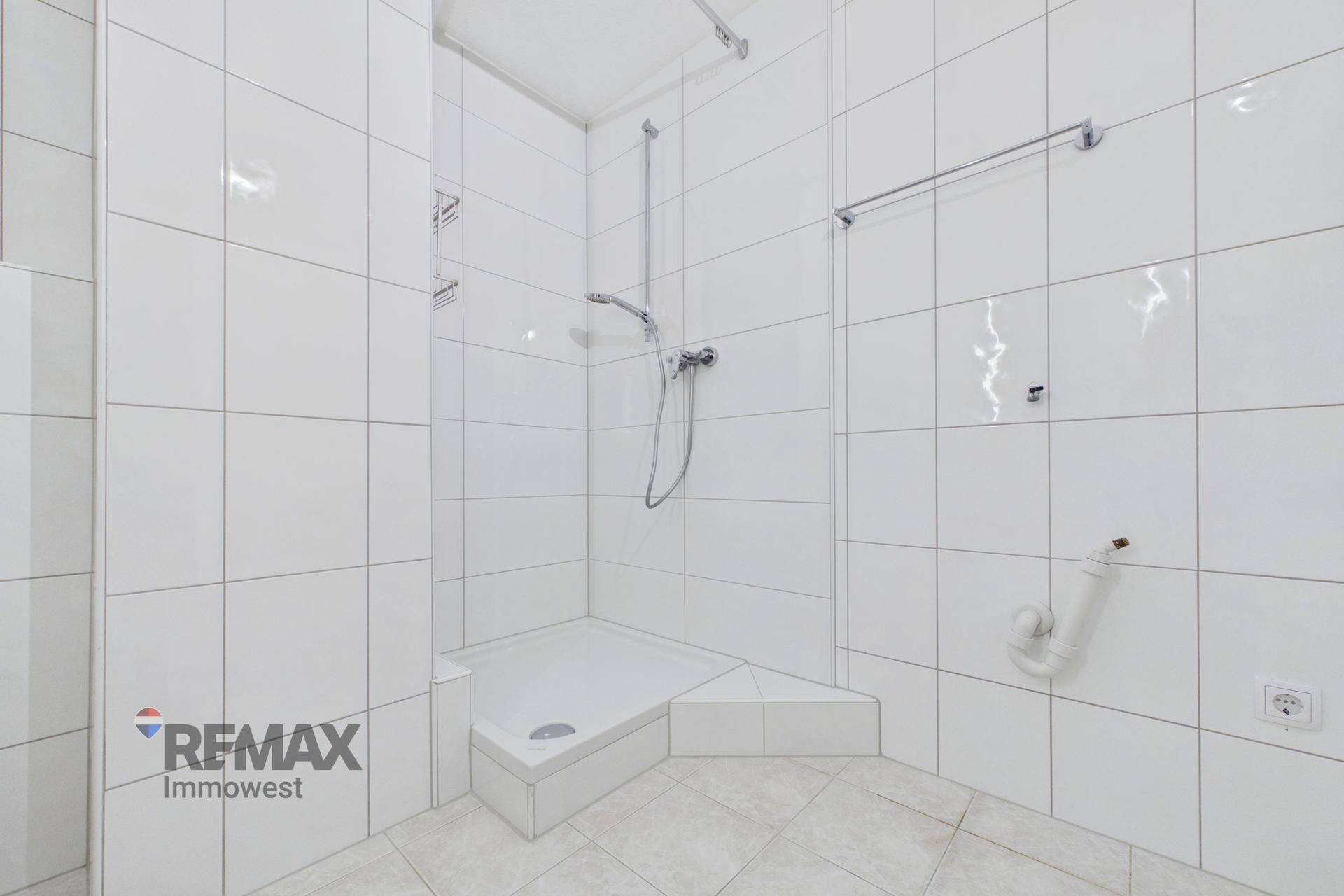 Weiß geflieste Dusche mit Duschwanne und Armaturen in einem hellen Badezimmer.