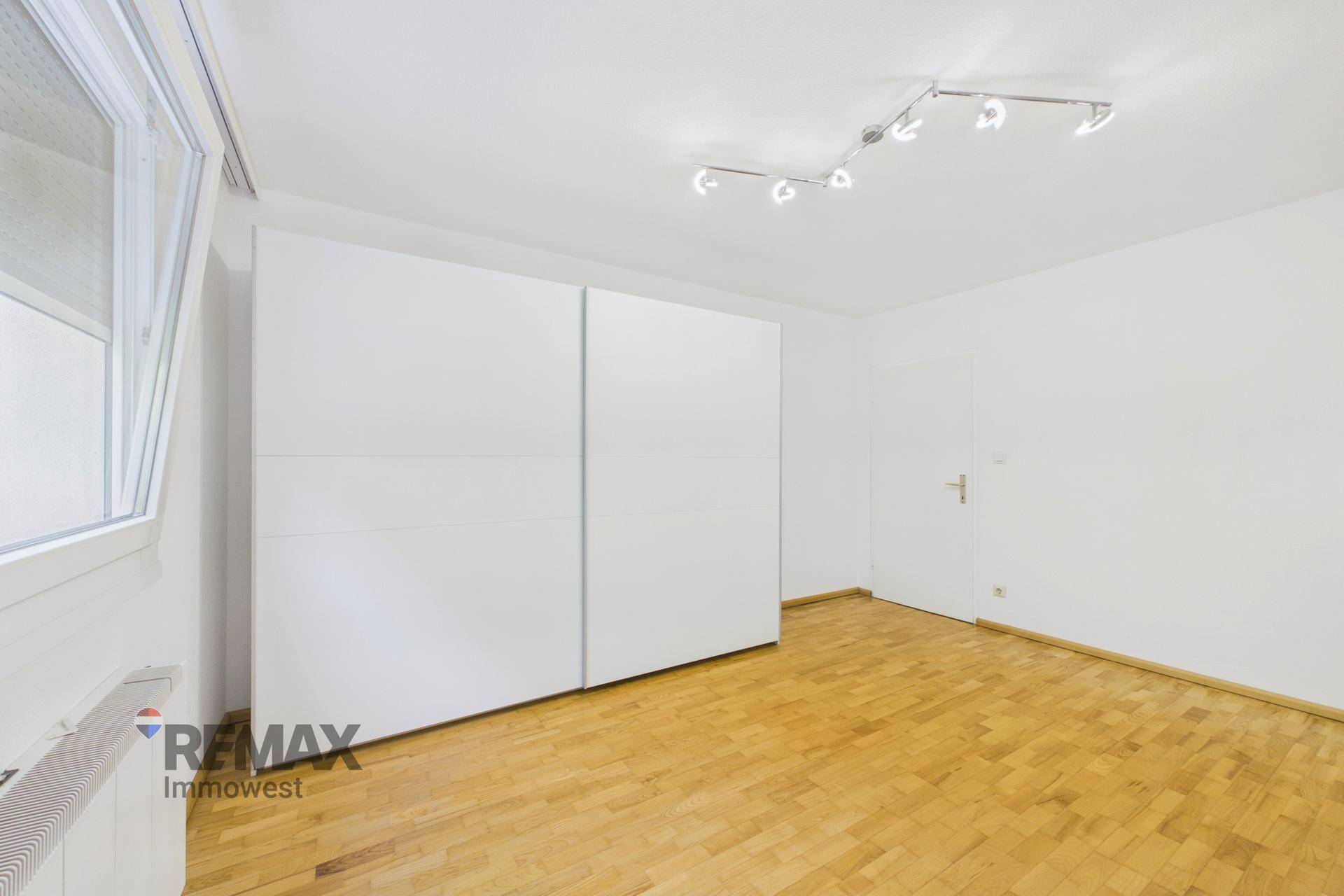 Schlafzimmer mit Parkettboden und einem großen weißen Schiebetürenschrank.