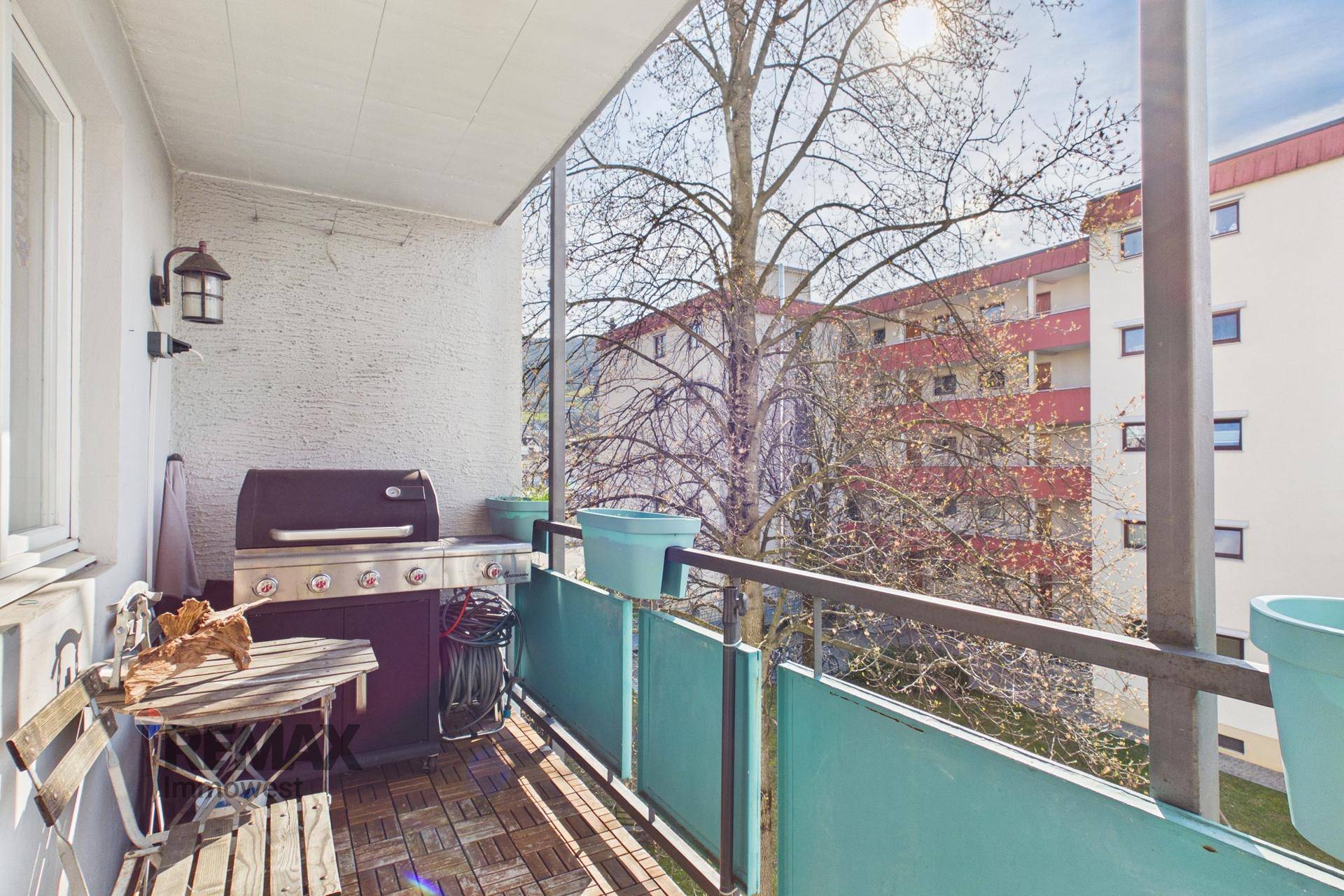Gemütlicher Balkon mit Grill, Holzbodenfliesen und Blick auf die Umgebung.
