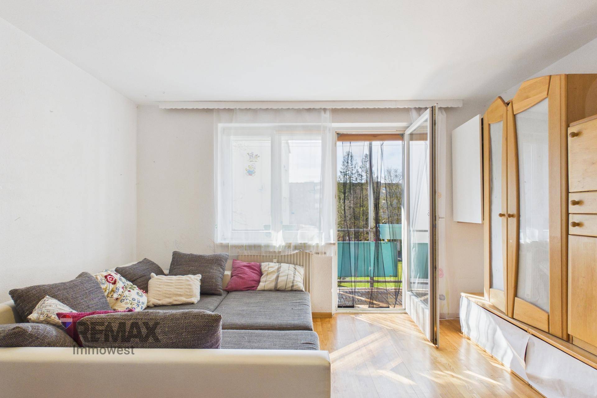 Wohnzimmer mit Sofa, hellem Parkettboden und direktem Zugang zum Balkon.