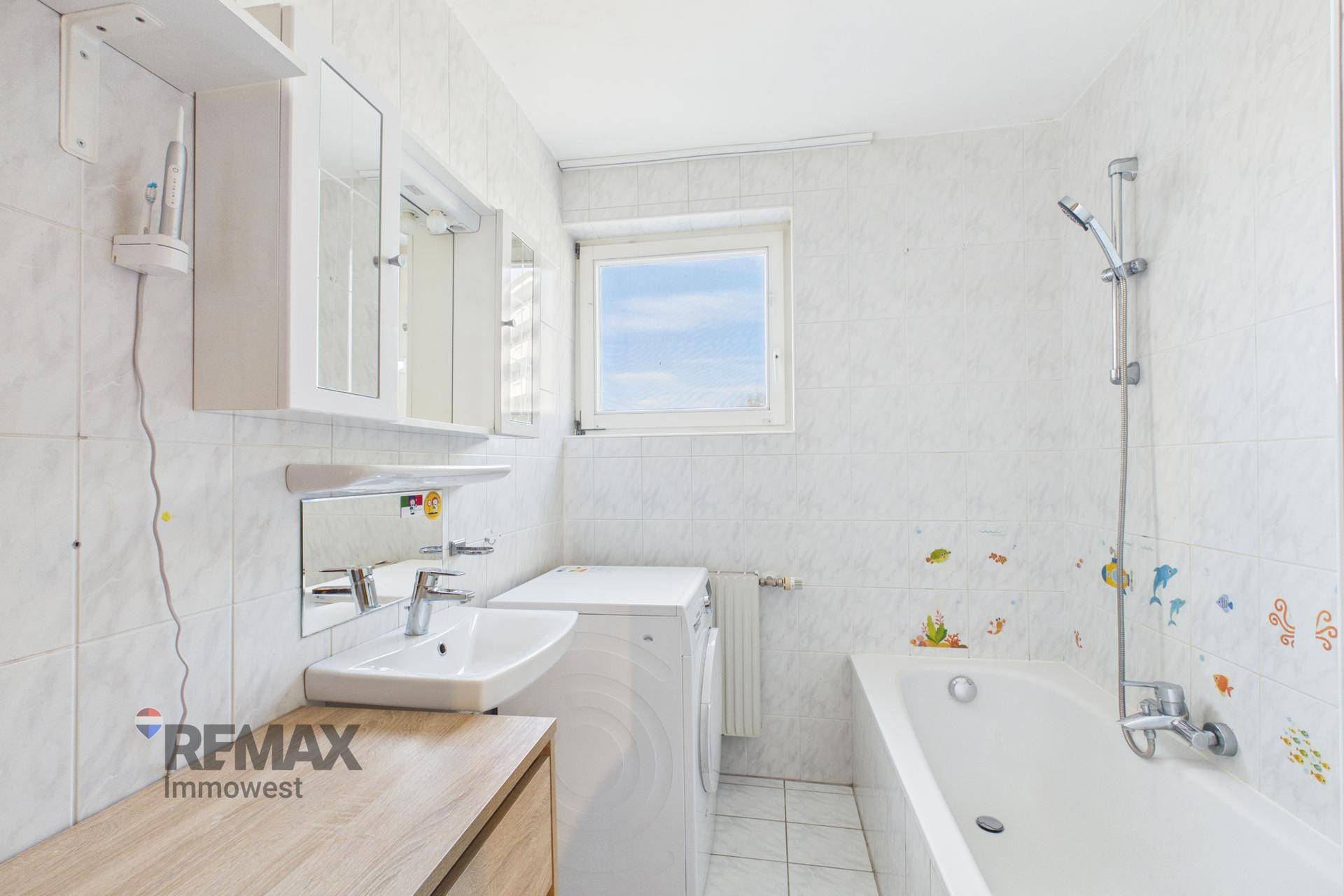 Badezimmer mit Badewanne, Waschbecken, Waschmaschine und Fenster.