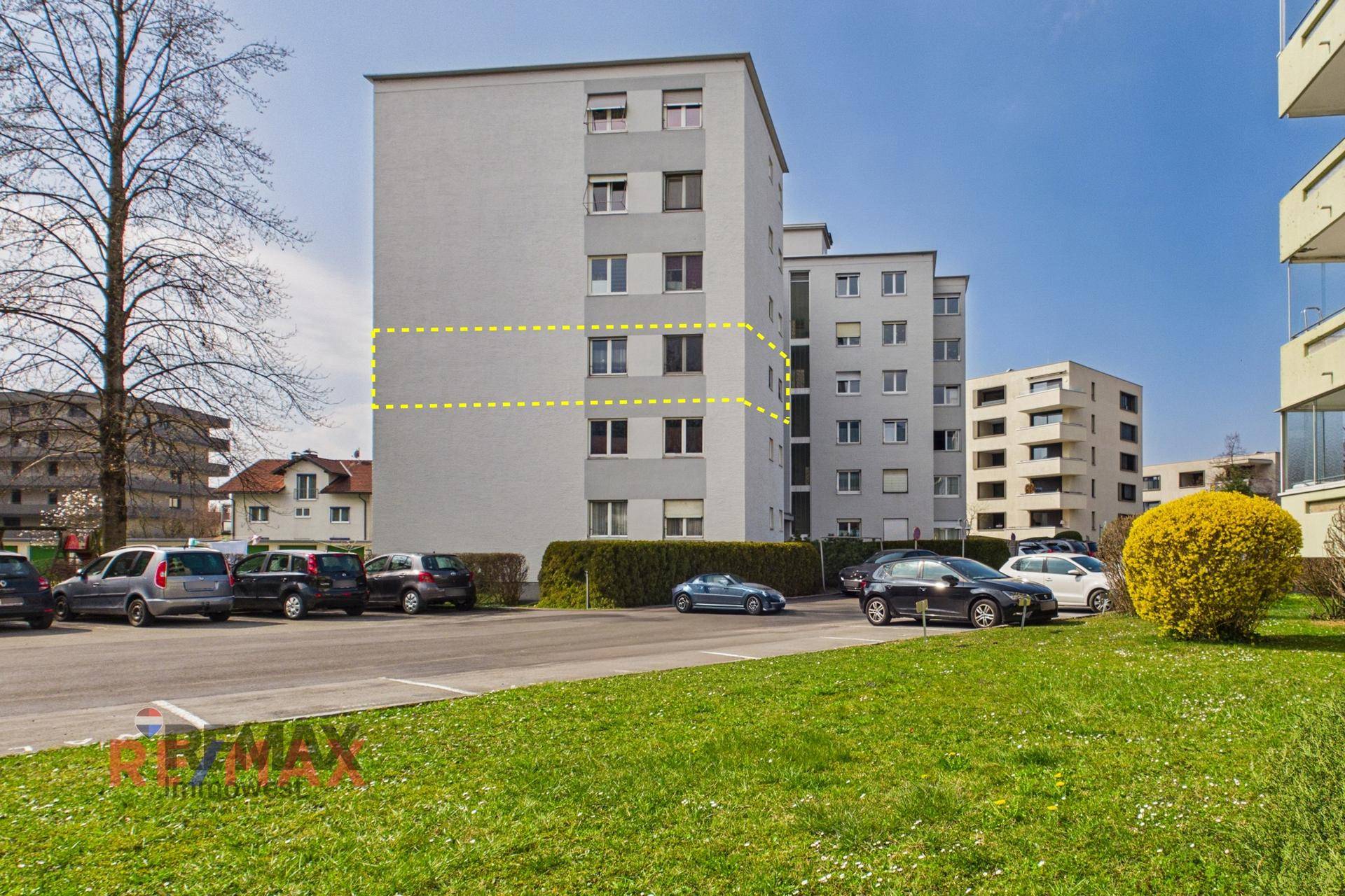Mehrfamilienhaus mit mehreren Etagen und Parkplätzen im Freien.