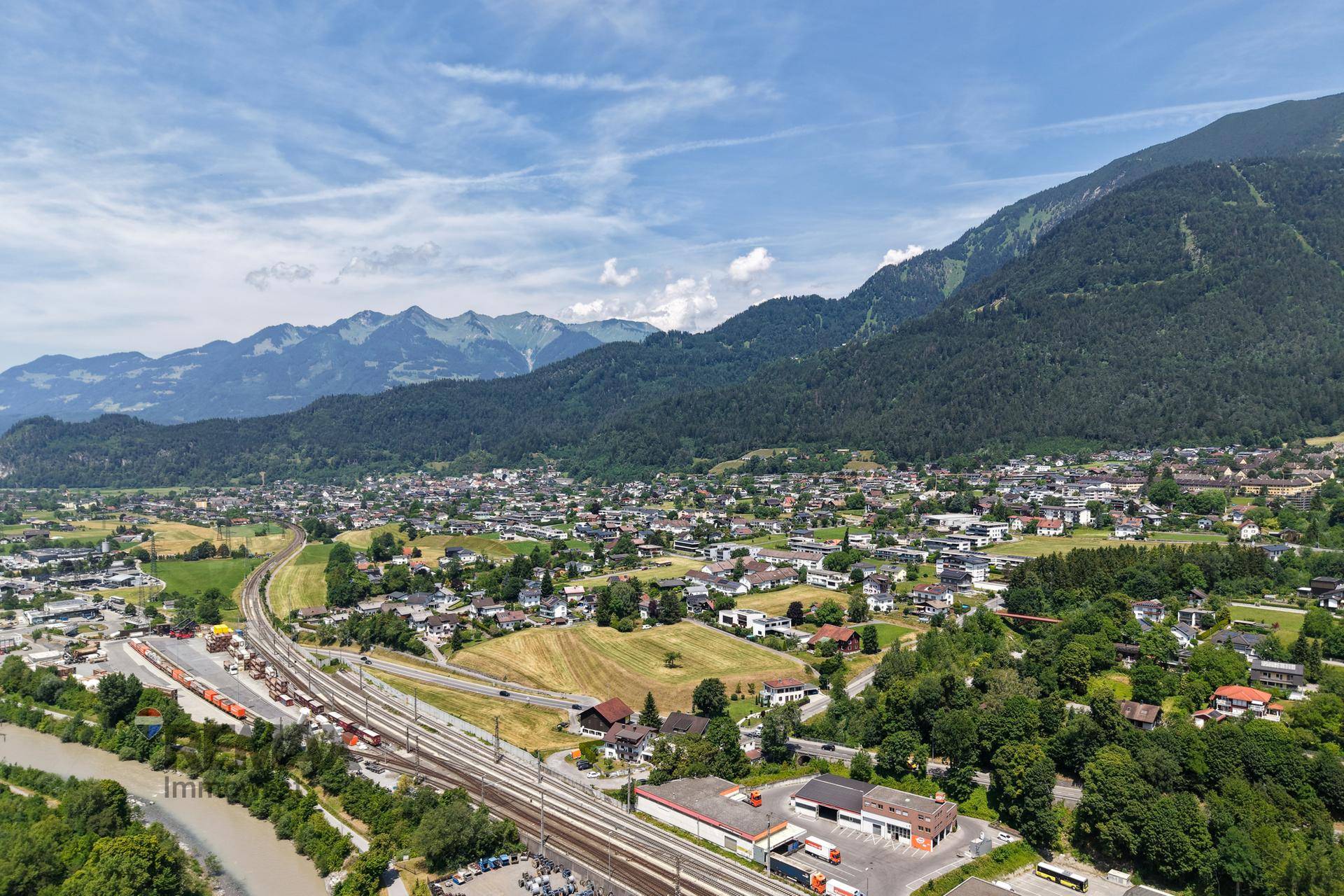 Panoramablick auf eine Stadt im Tal, umgeben von Bergen, mit Flüssen, Straßen und Bahngleisen.