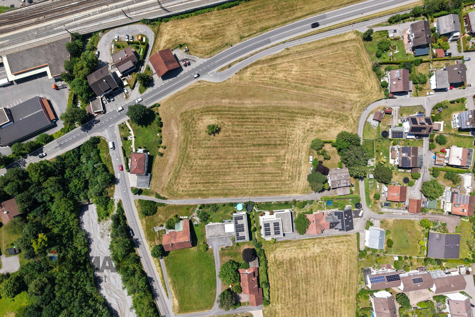 Senkrechte Luftaufnahme eines großen, grünen Feldes mit angrenzenden Straßen und Wohngebäuden.