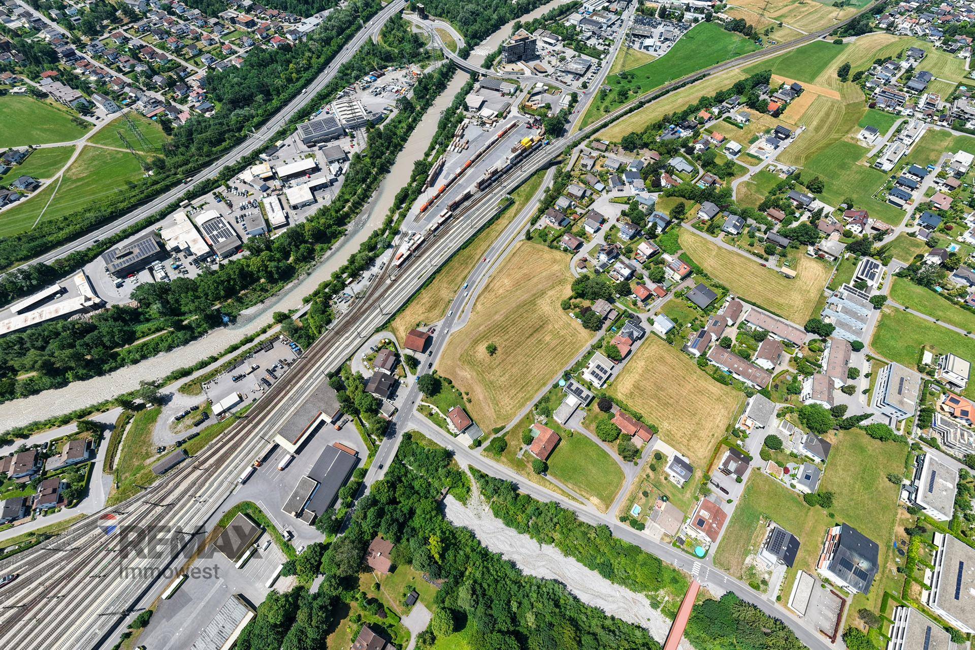 Panoramische Luftaufnahme einer Stadt mit Fluss, Bahngleisen und einer beeindruckenden Bergkulisse.
