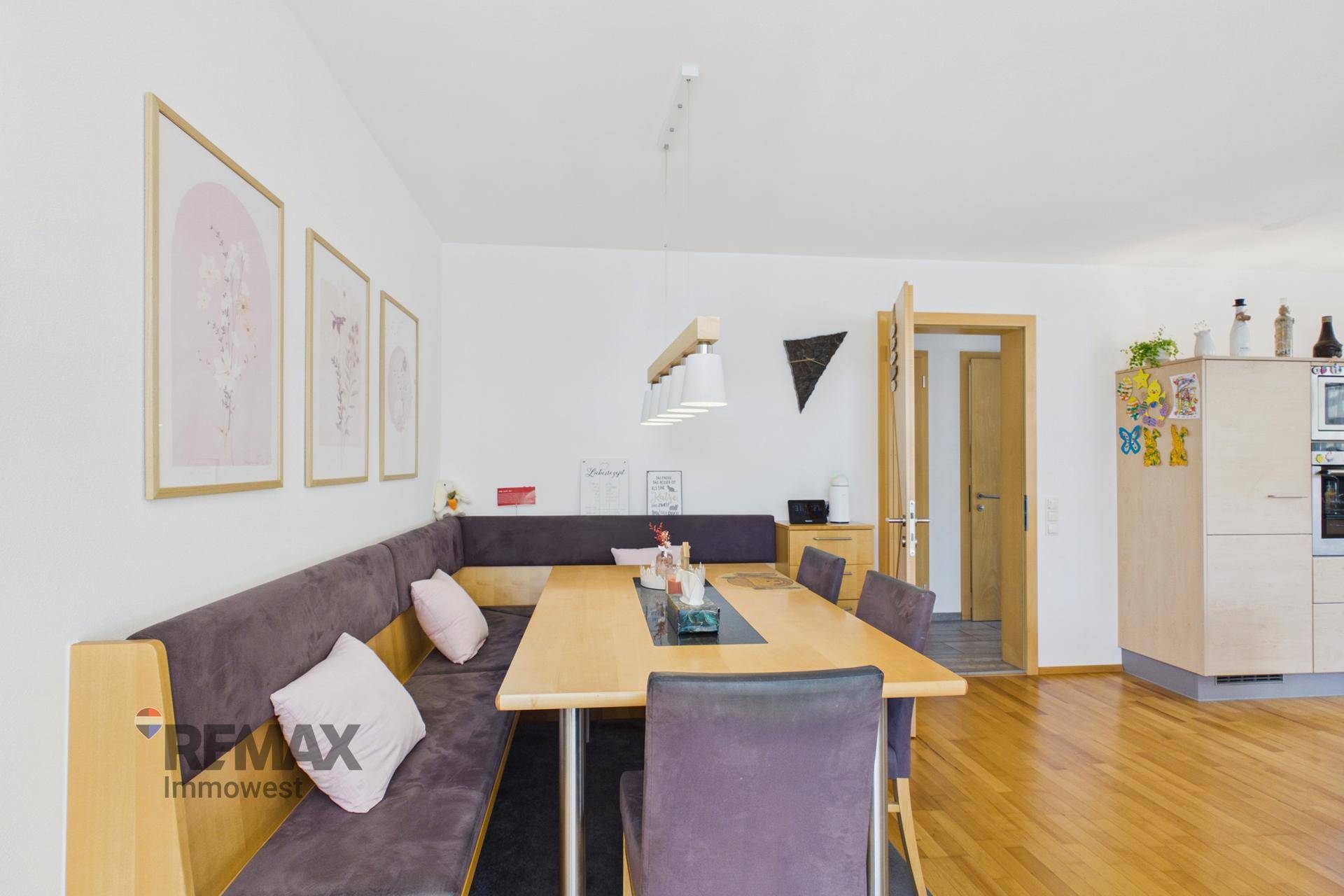 Gemütlicher Essbereich mit Eckbank, Holztisch und modernen Bildern an der weißen Wand.