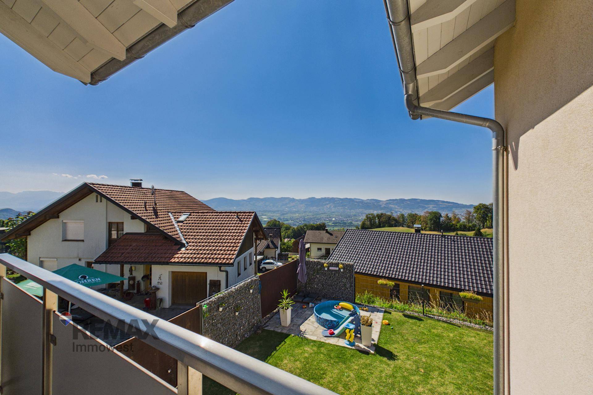 Blick vom Balkon auf den Garten mit kleinem Pool und Spielgeräten sowie weitreichender Fernsicht.