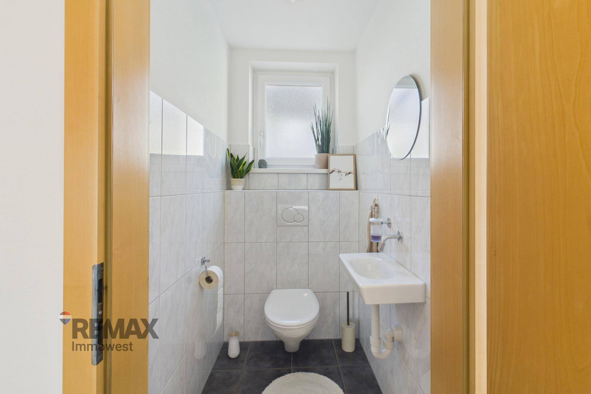 Modernes Gäste-WC mit Wand-WC, kleinem Waschbecken und Fenster für Tageslicht.