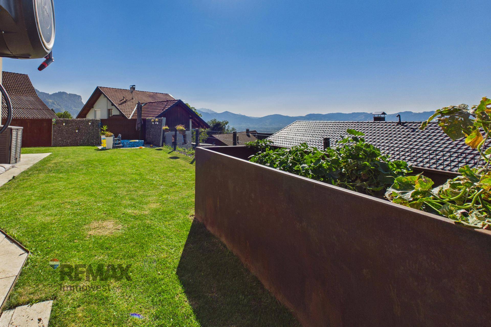 Gepflegter Garten mit Hochbeet, Rasenfläche und weitem Blick auf die Landschaft.