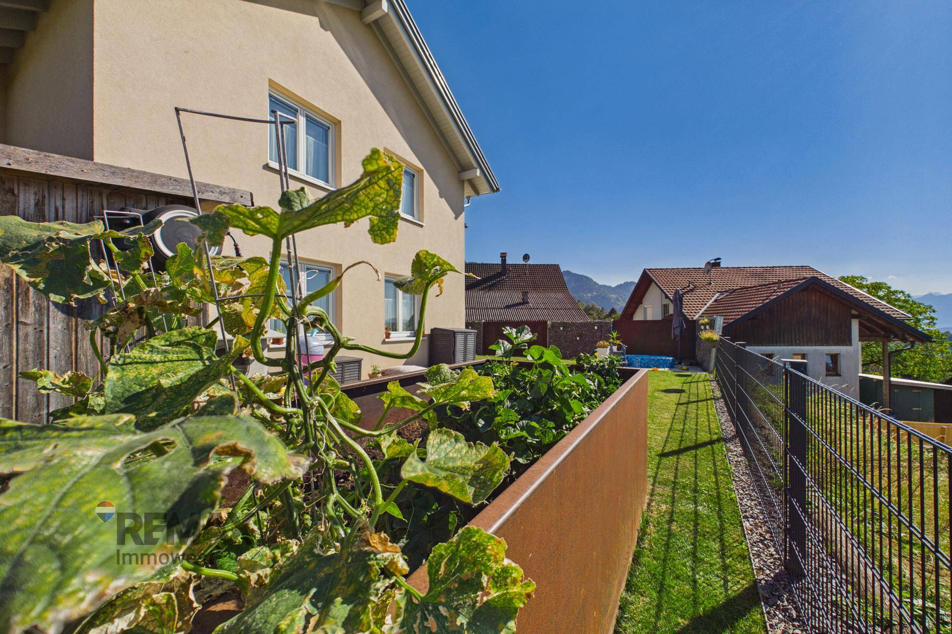 Gartenbereich mit Hochbeet für Pflanzen, Zaun und Blick auf die umliegende Natur.