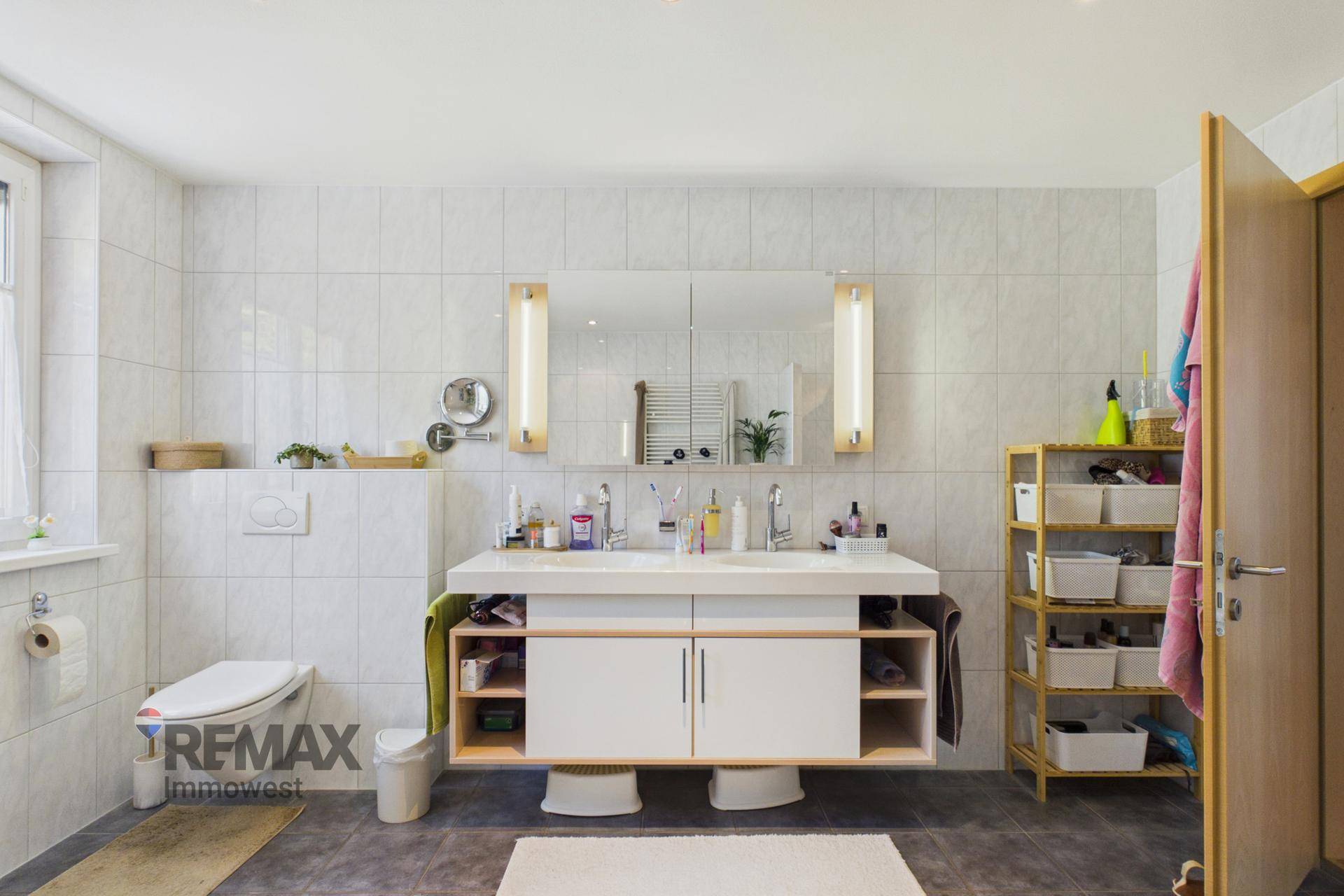 Geräumiges Badezimmer mit Doppelwaschbecken, Spiegelschrank und wandhängendem WC.