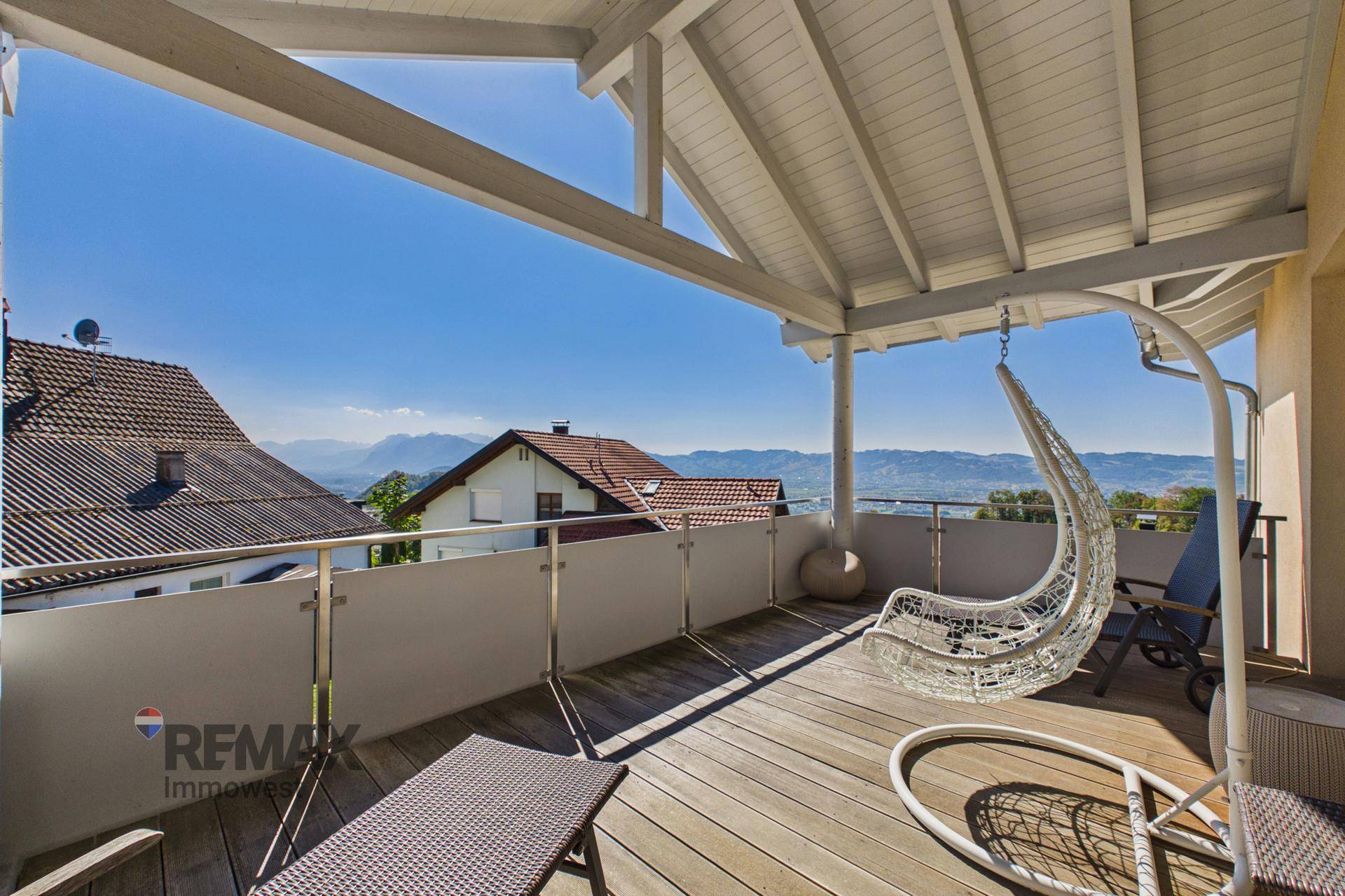 Großer überdachter Balkon mit Holzboden, Hängesessel und weitem Bergblick.