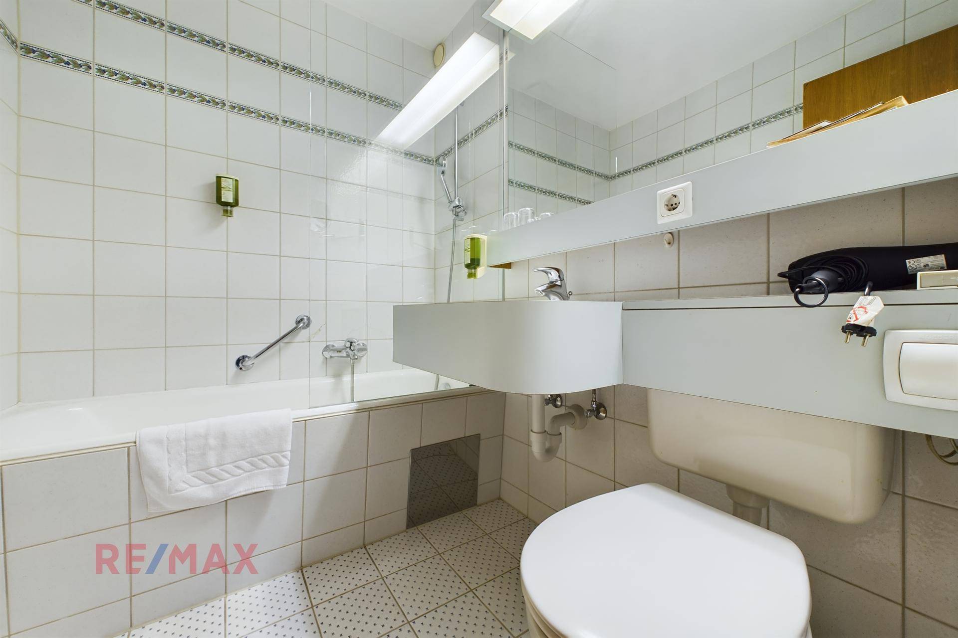 Helles Badezimmer mit Badewanne, WC und Waschbecken, komplett gefliest in Weiß.