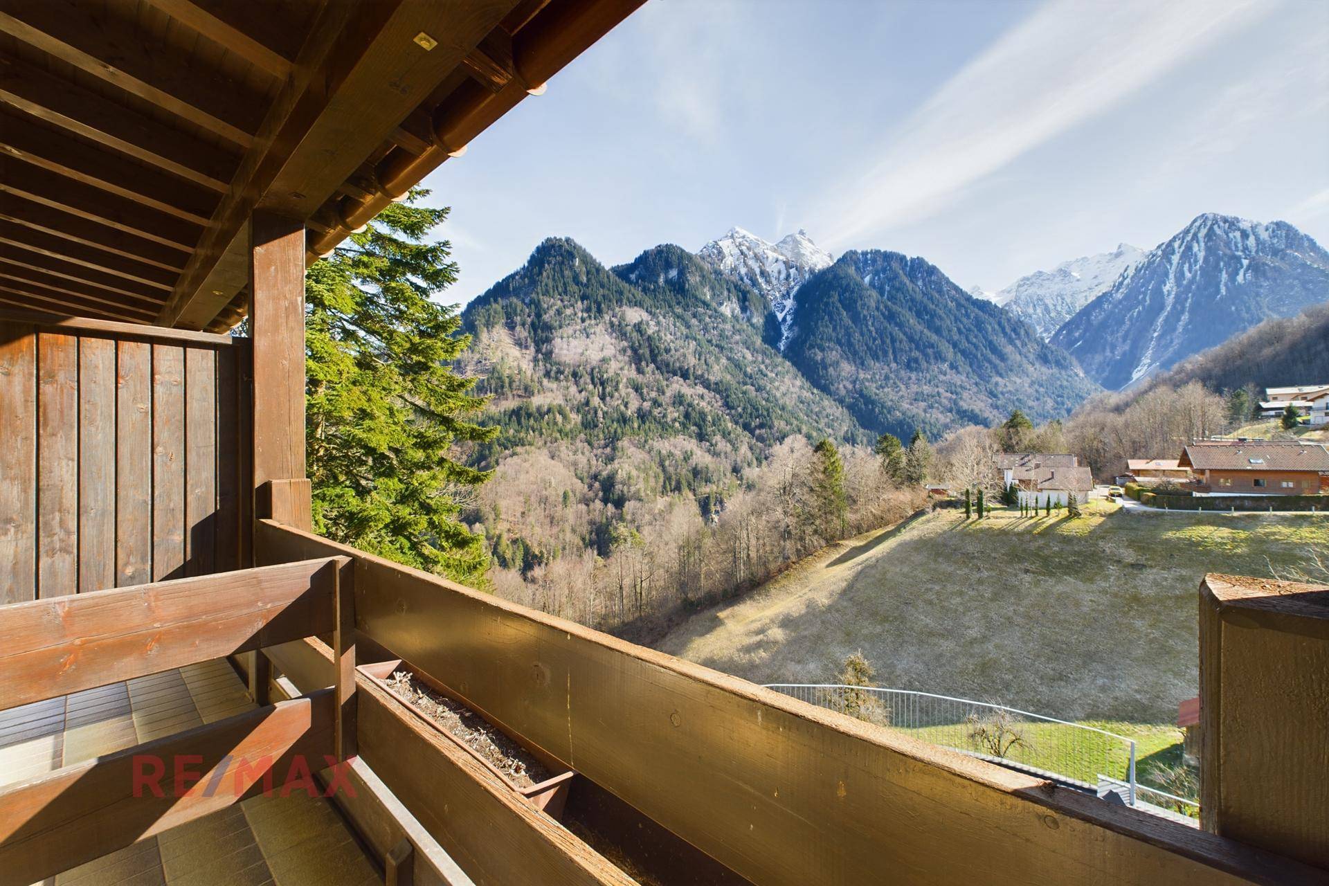 Holzbalkon mit Blick auf die bewaldeten Berge und die umliegende Landschaft unter blauem Himmel.