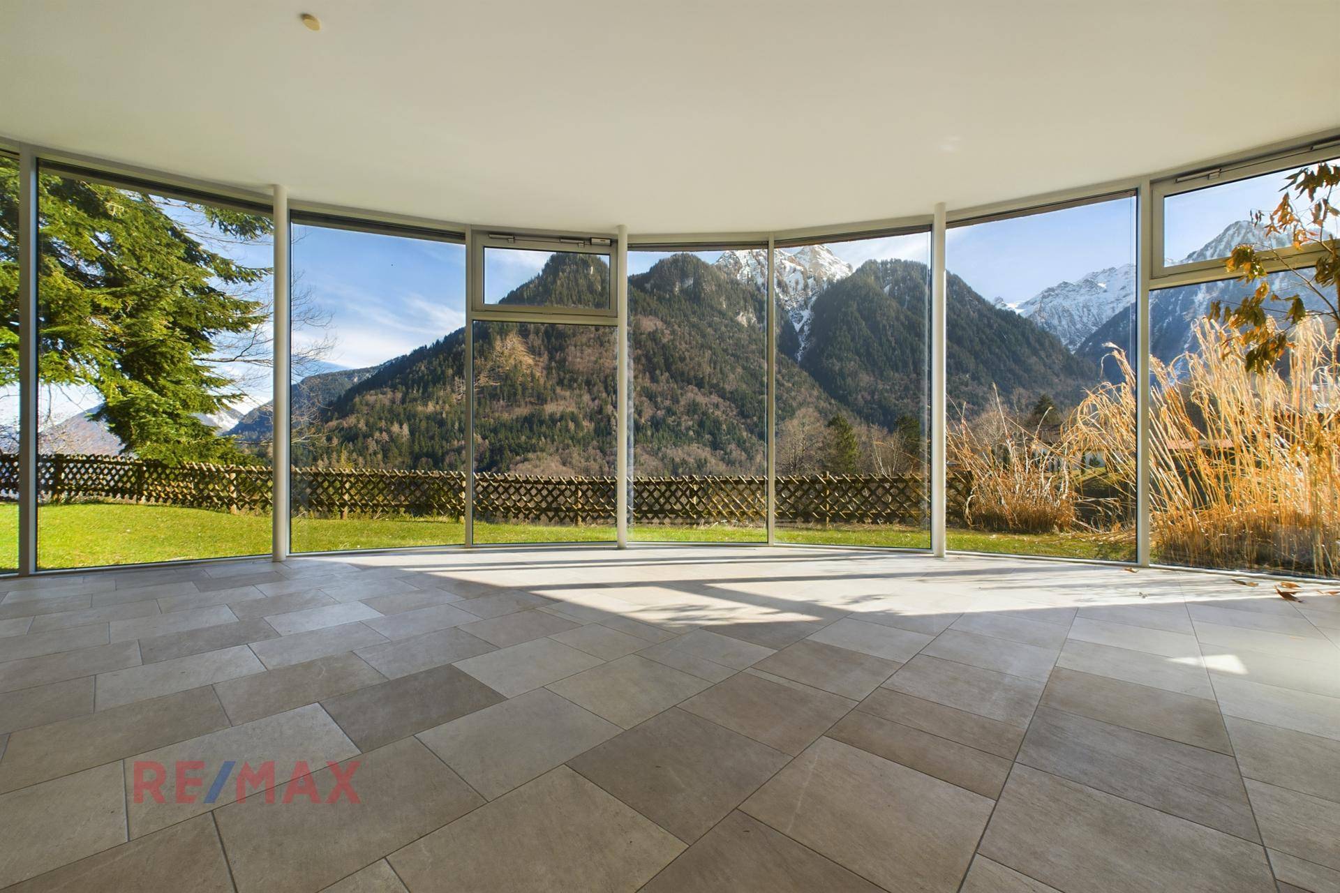 Heller Wintergarten mit großen Panoramafenstern, die einen weiten Blick auf die Berge bieten.