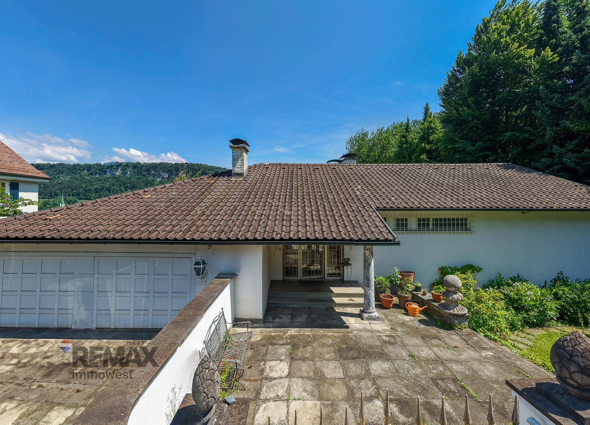 Eingangsbereich des Hauses mit Garage und gepflastertem Vorplatz, umgeben von Grün.