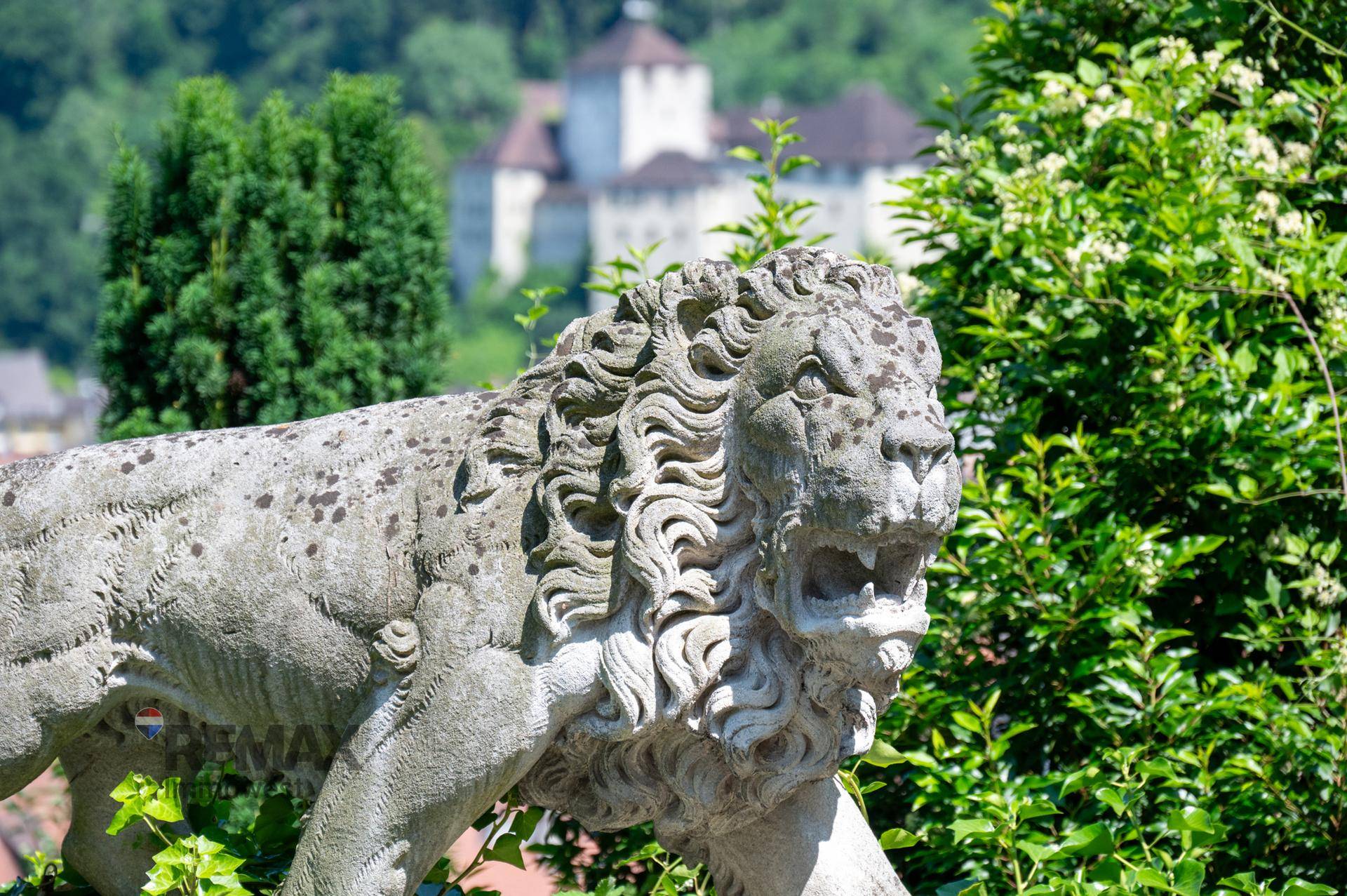 Detailansicht einer Löwenstatue im Garten mit einer historischen Burg im Hintergrund.