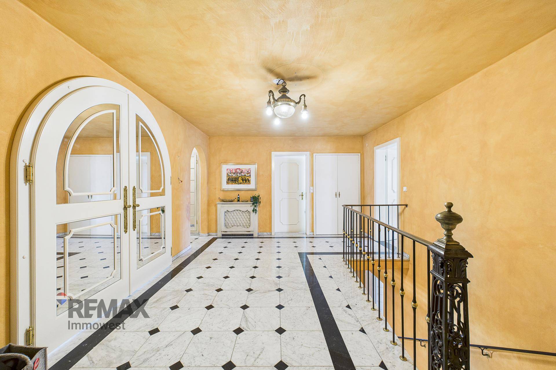 Geräumiger Flur mit gelben Wänden, schwarz-weißem Marmorboden und eleganter Treppe.