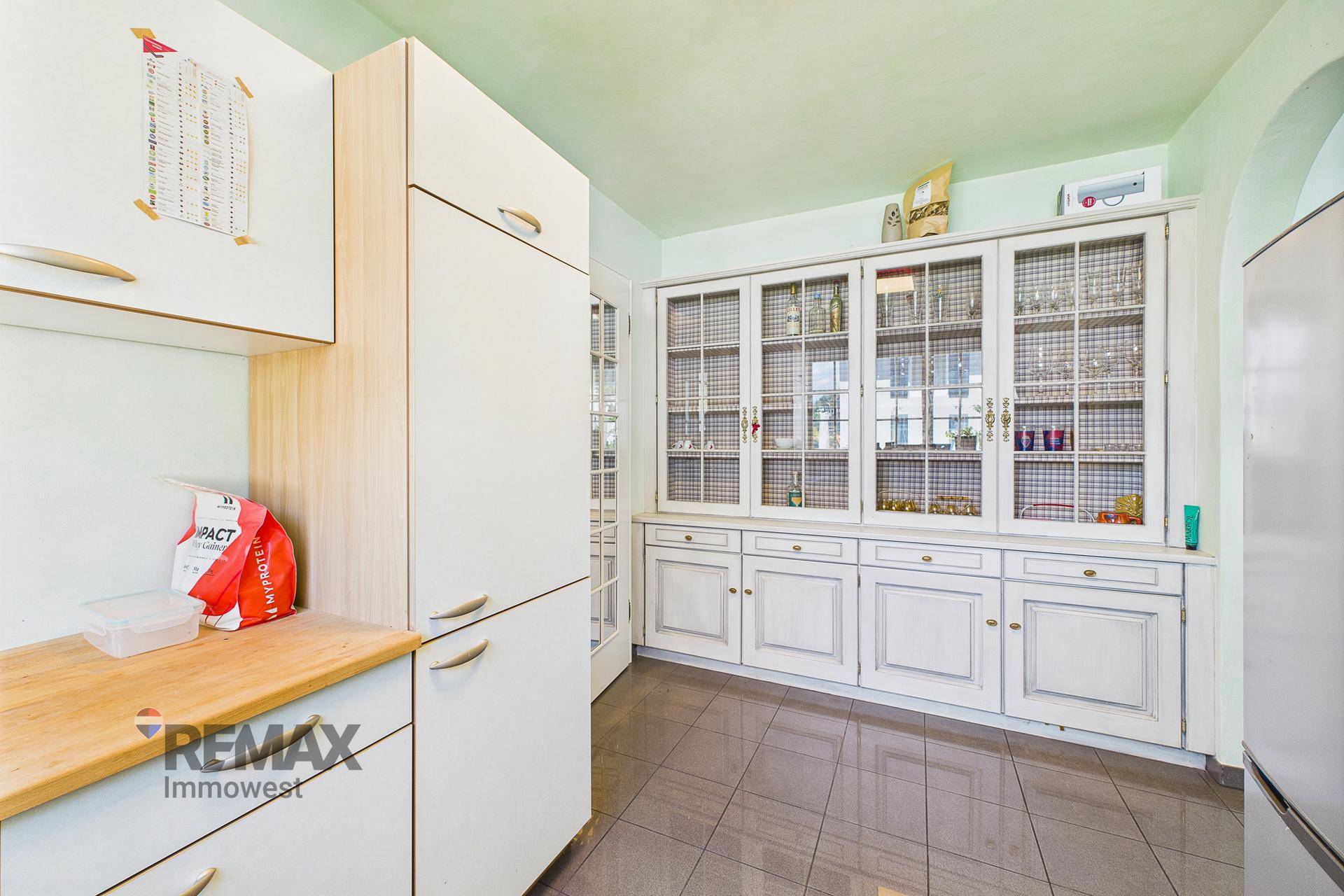Küchenbereich mit weißen Schränken, Holztheke und einem großen Vitrinenschrank.