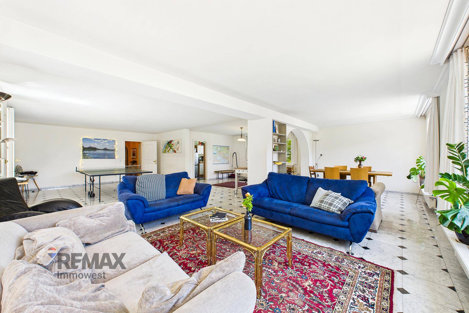 Großzügiger offener Wohn- und Essbereich mit Marmorboden und blauen Sofas.