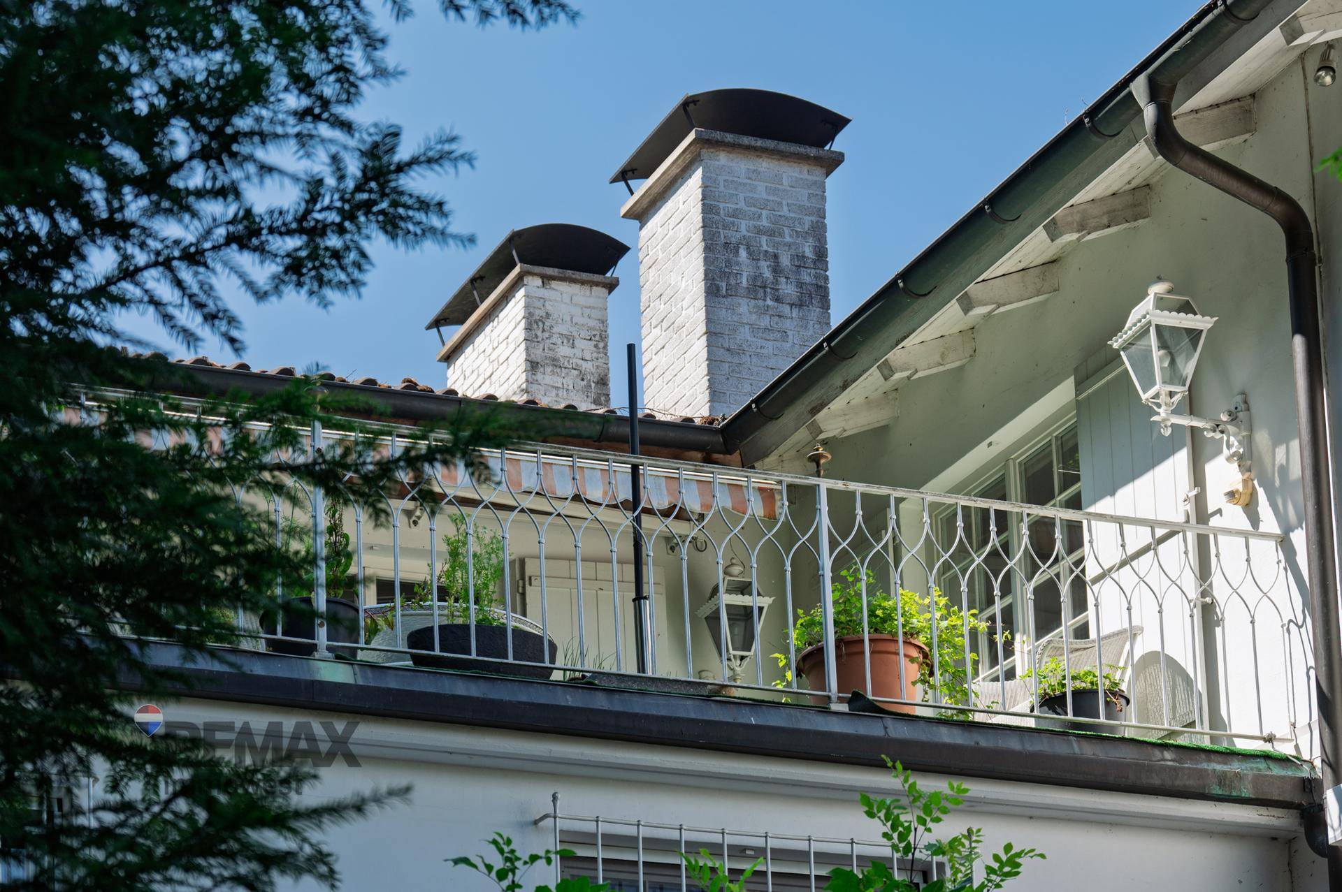 Kleiner Balkon mit schmiedeeisernem Geländer und Pflanzen, unter einem blauen Himmel.