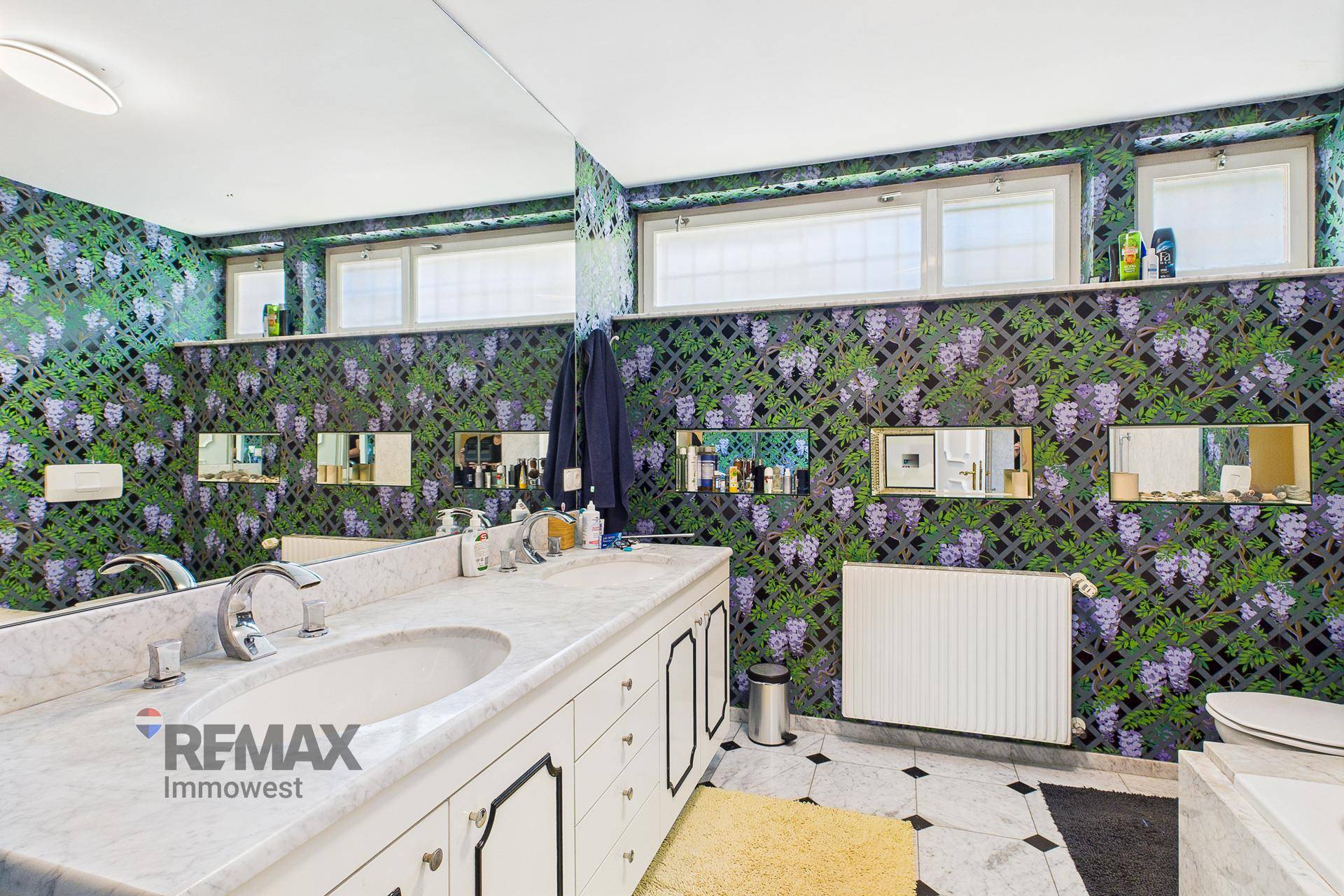 Geräumiges Badezimmer mit floraler Tapete, Doppelwaschbecken und Marmoroberflächen.