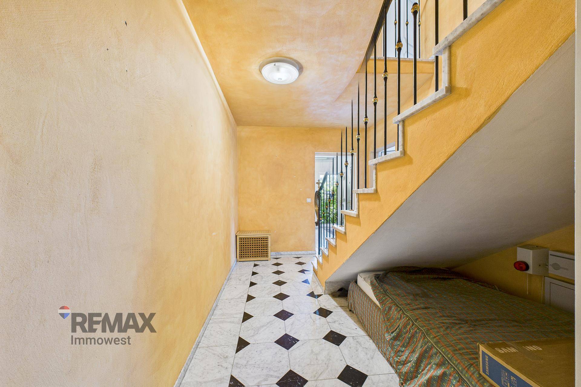 Treppenhaus mit gelben Wänden und schwarz-weißem Marmorboden, führt in die obere Etage.