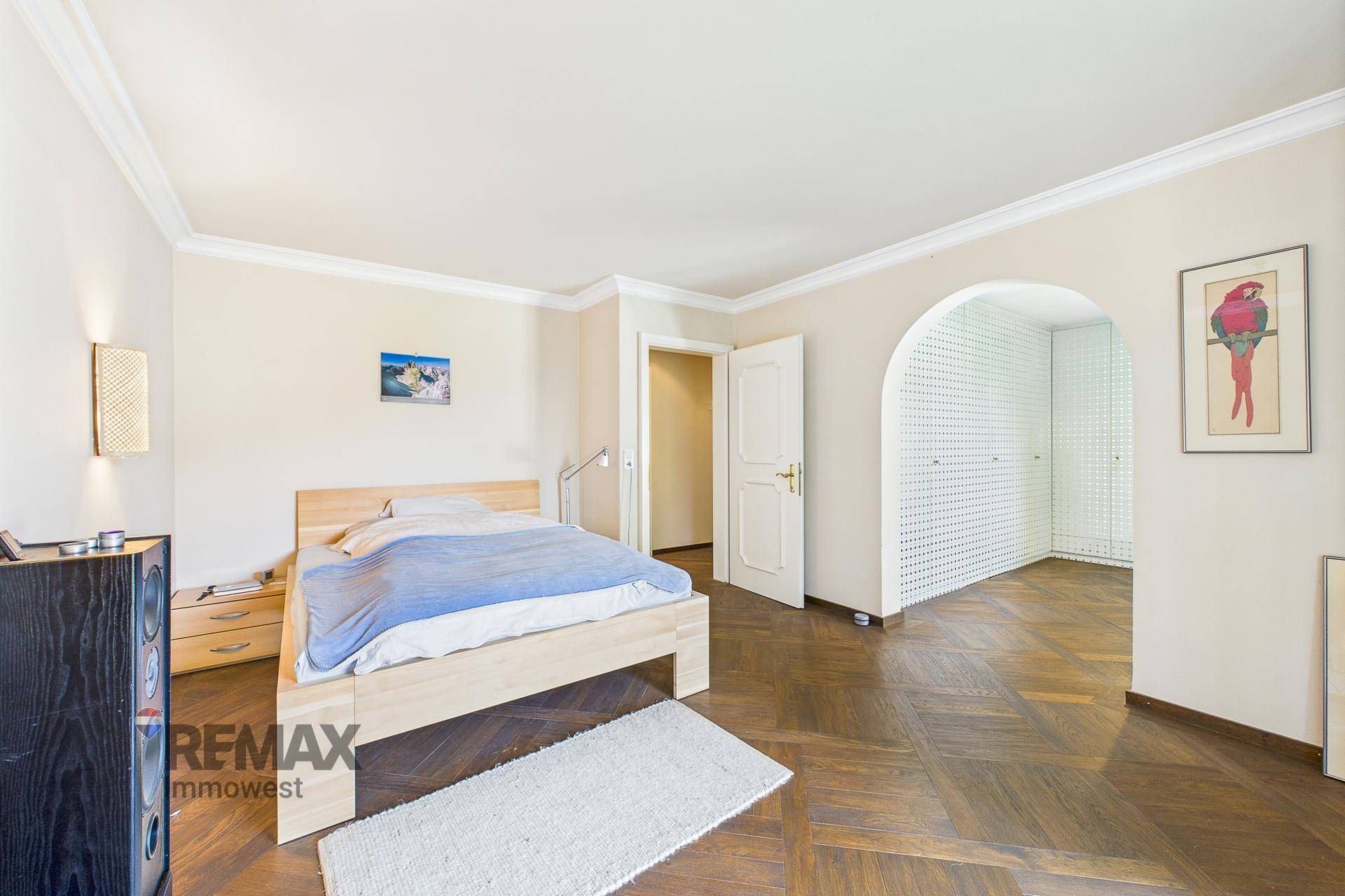 Helles Schlafzimmer mit Holzbett, Parkettboden und einem offenen Durchgang zu einem Ankleidebereich.