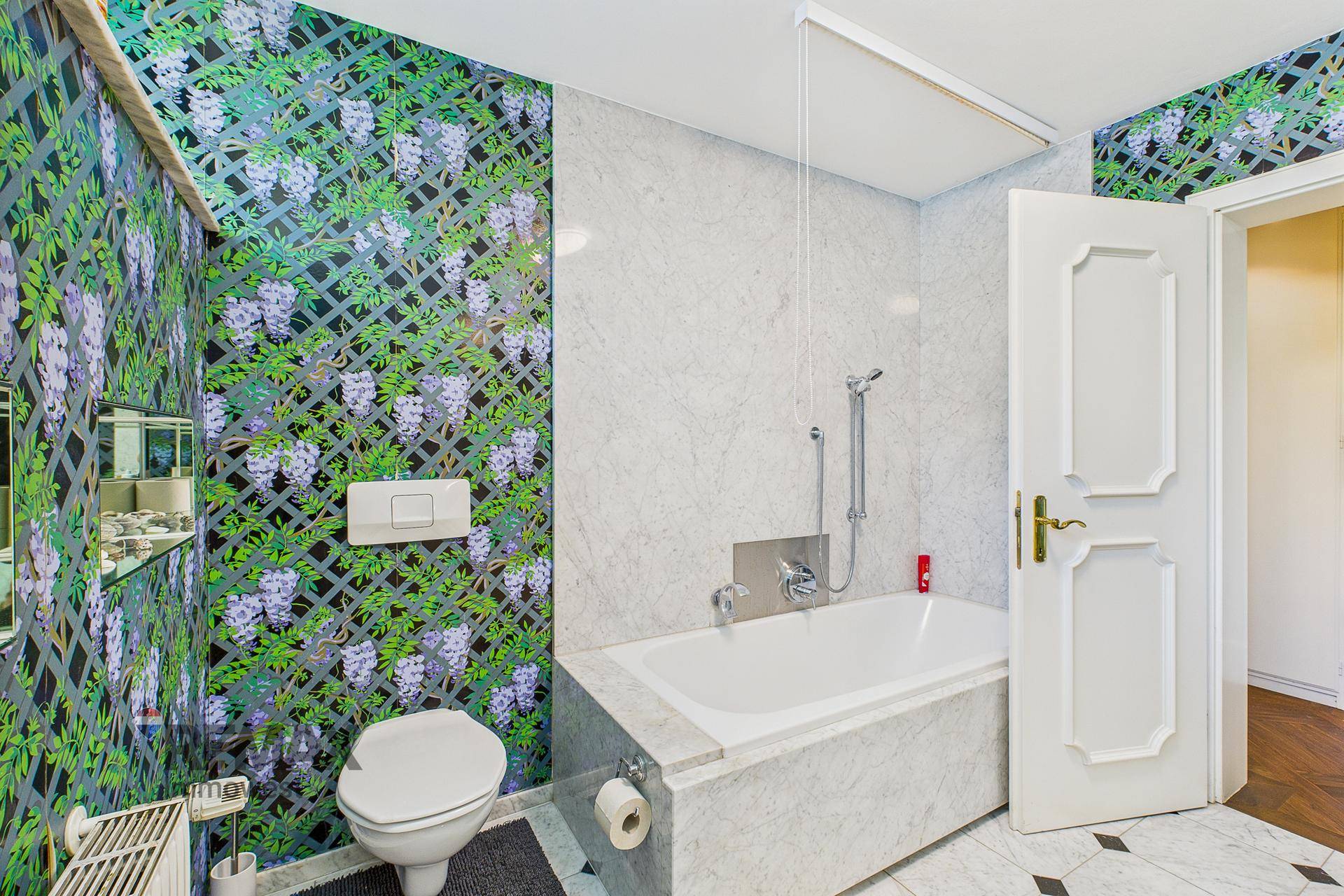 Badezimmer mit floraler Tapete, Badewanne und wandmontierter Toilette.