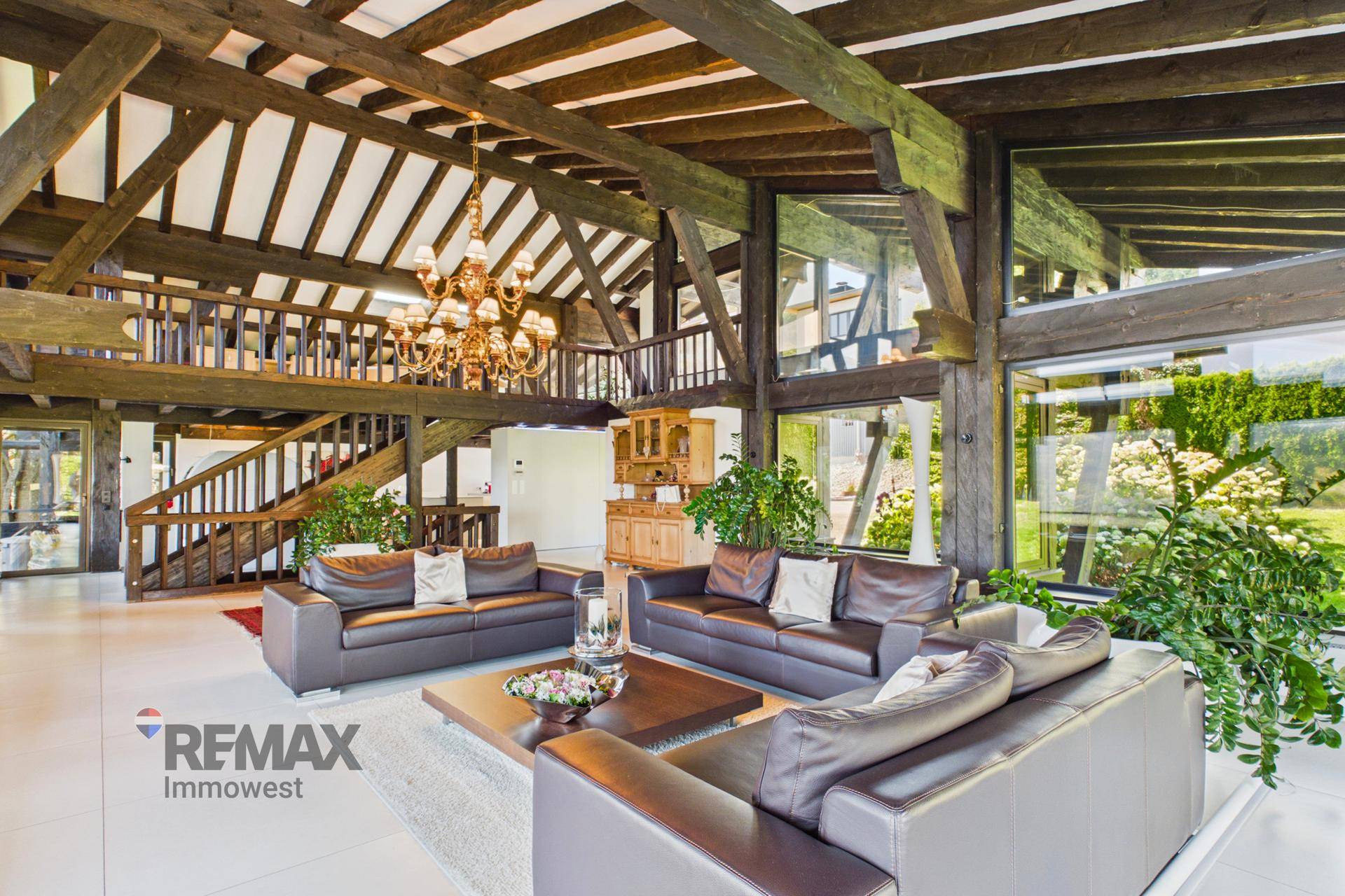 Geräumiges Wohnzimmer mit hohen Decken, sichtbaren Holzbalken und eleganter Kronleuchterbeleuchtung.