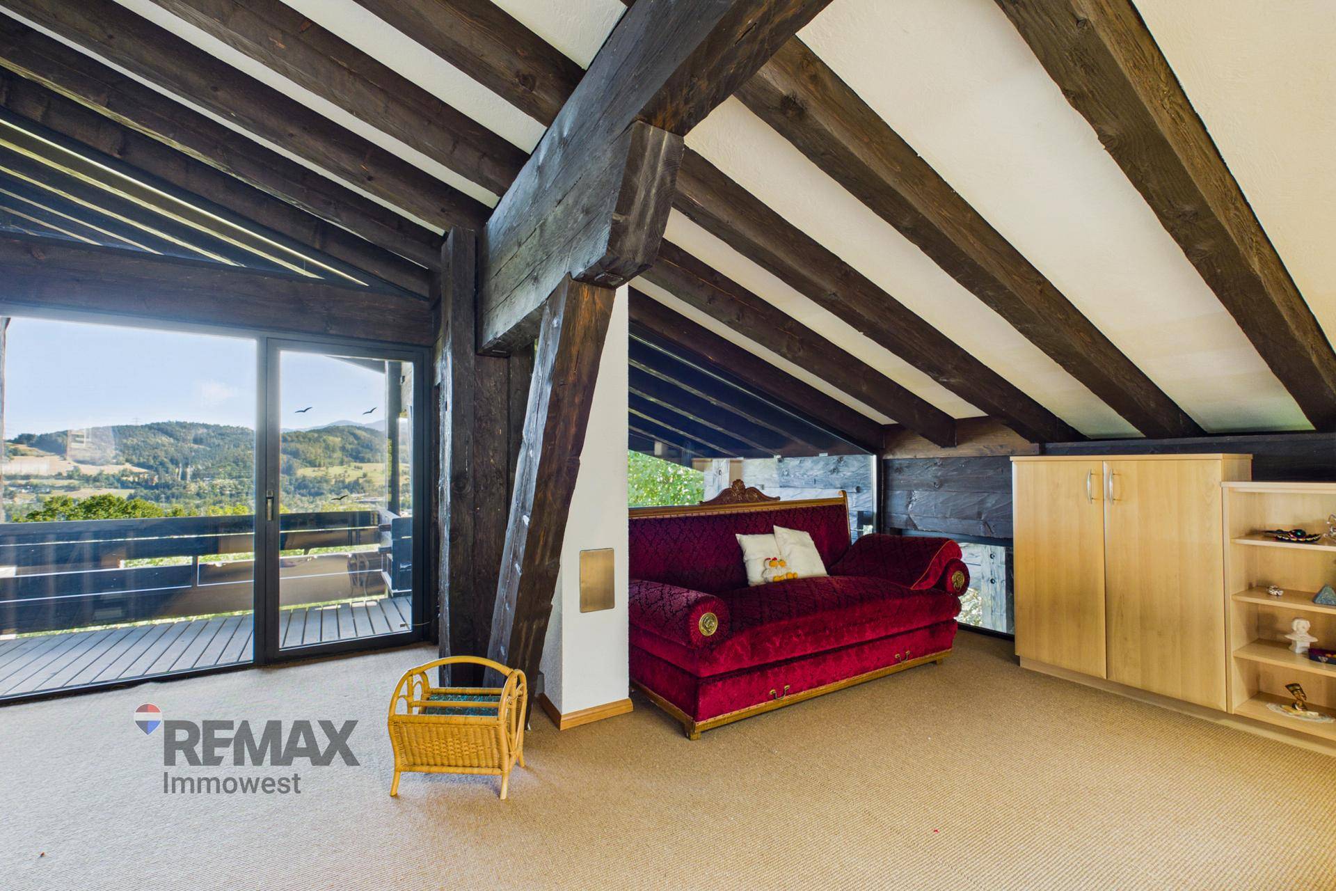Gemütliches Schlafzimmer im Dachgeschoss mit schrägen Decken, Holzbalken und Zugang zum Balkon.