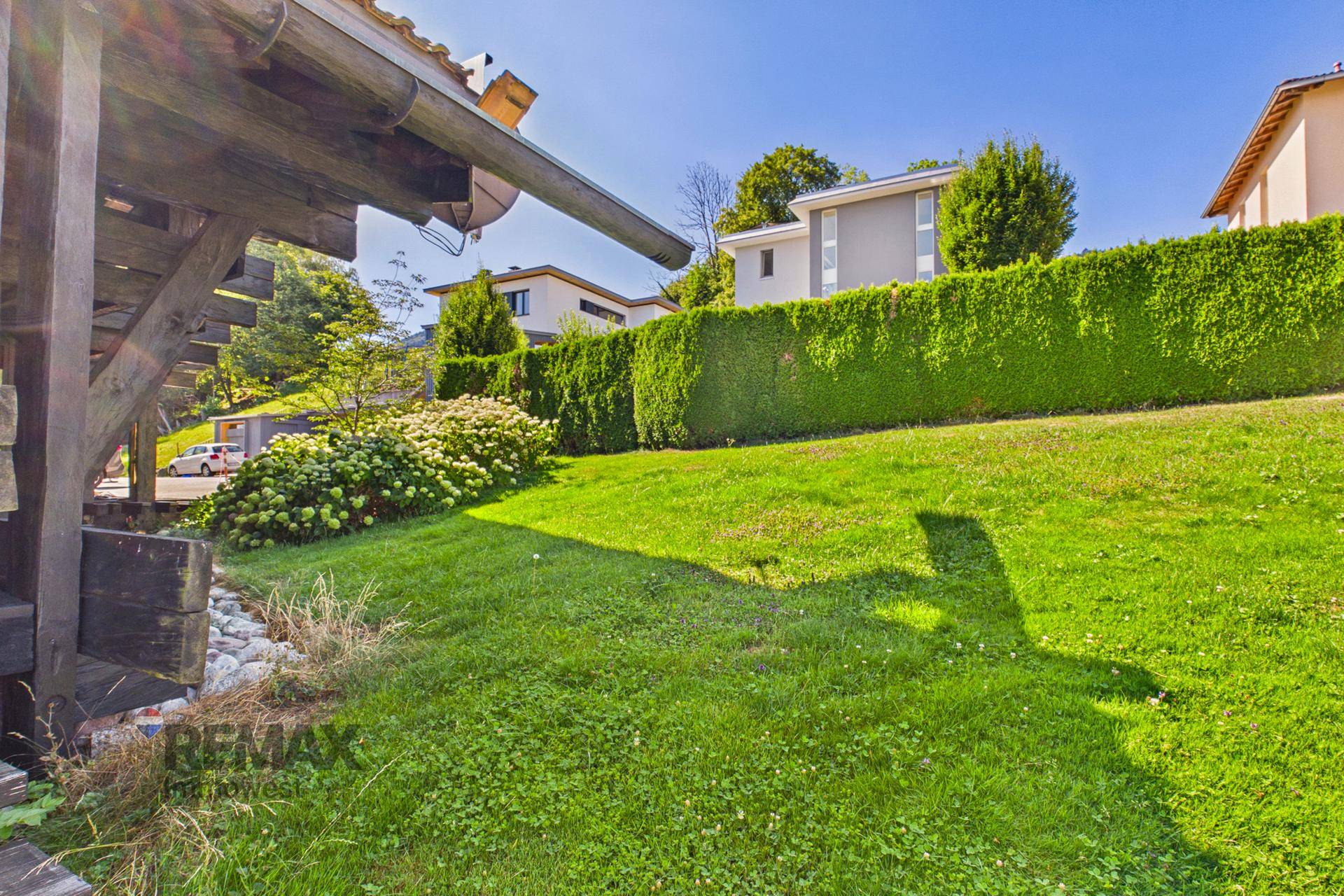 Großer, gepflegter Rasenbereich mit Hecke und Blick auf benachbarte Häuser.