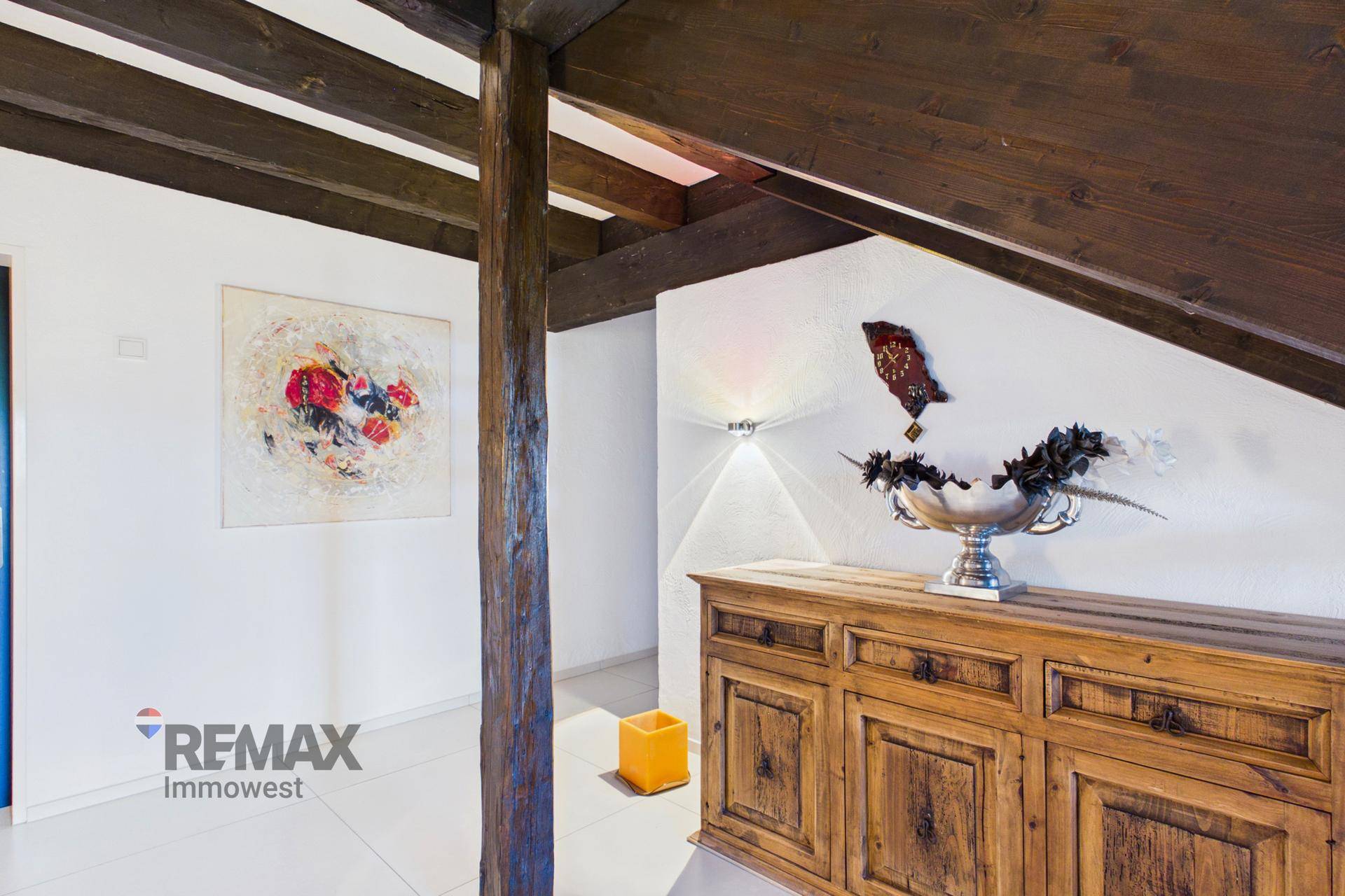 Flur mit rustikalem Holzschrank, Kunstwerken und sichtbaren Holzbalken an der Decke.