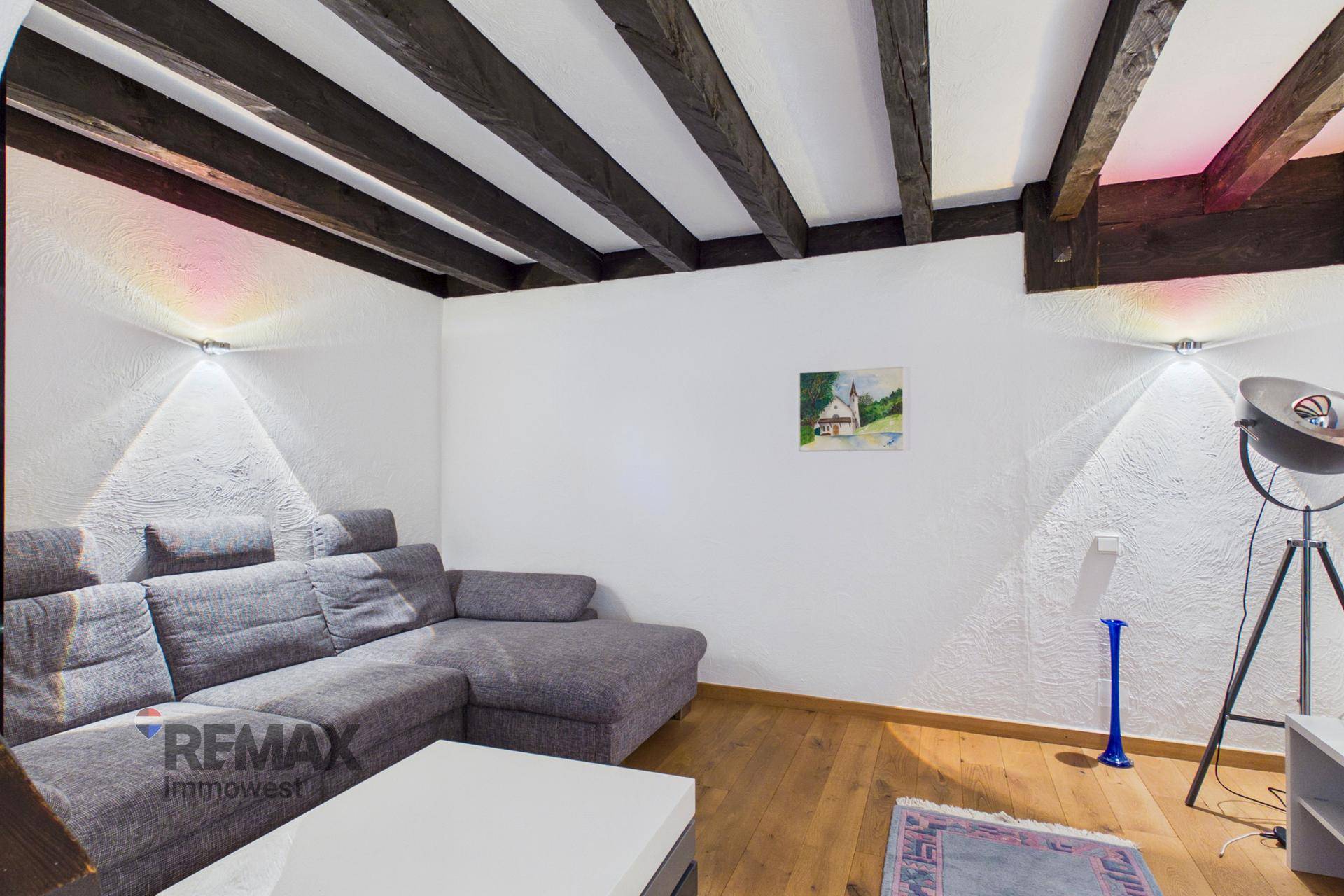 Gemütliches Wohnzimmer mit Ecksofa, Holzbalken und indirekter Beleuchtung.