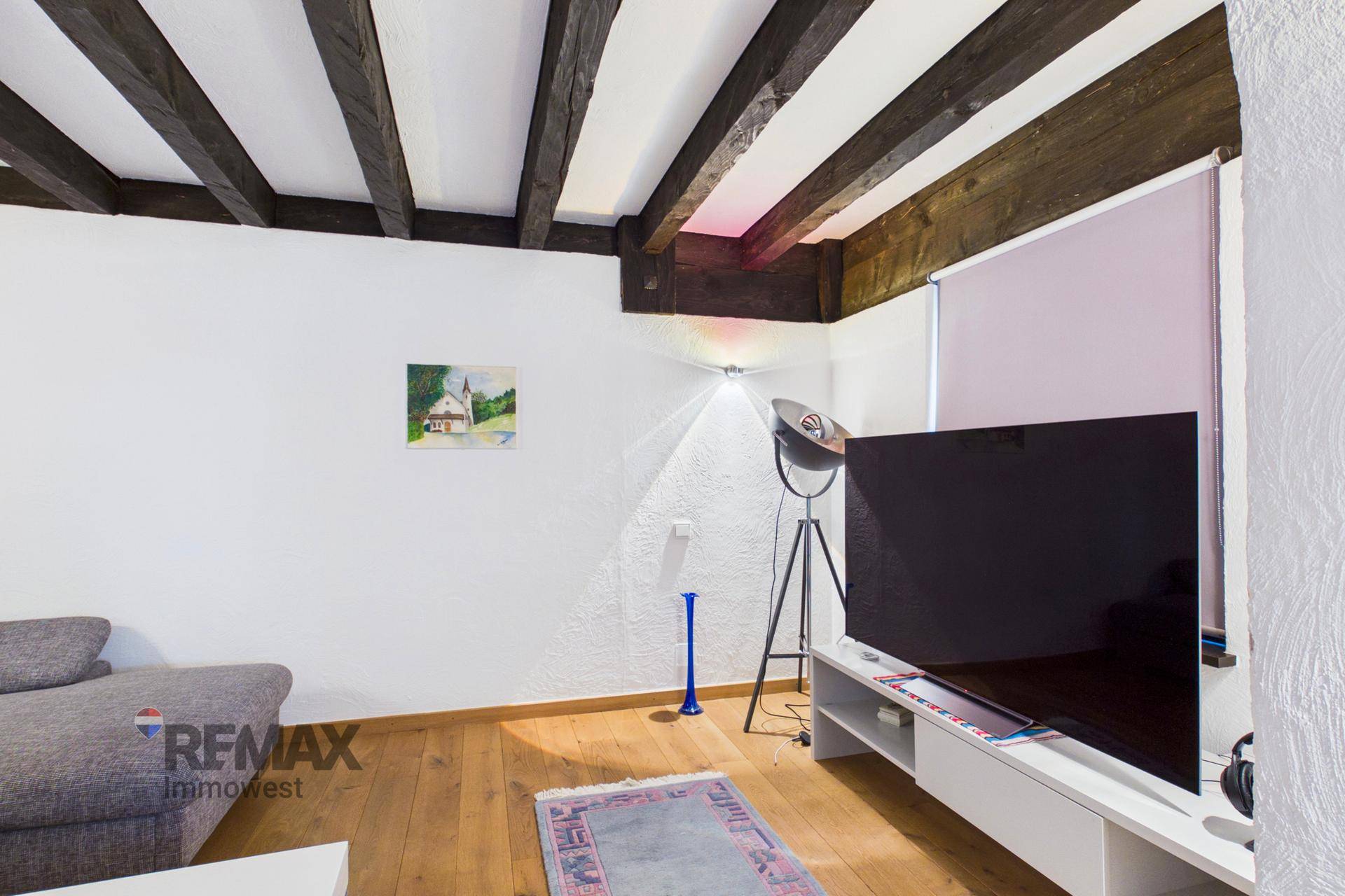 Wohnzimmer mit großem Fernseher, Ecksofa und Holzbalkendecke.