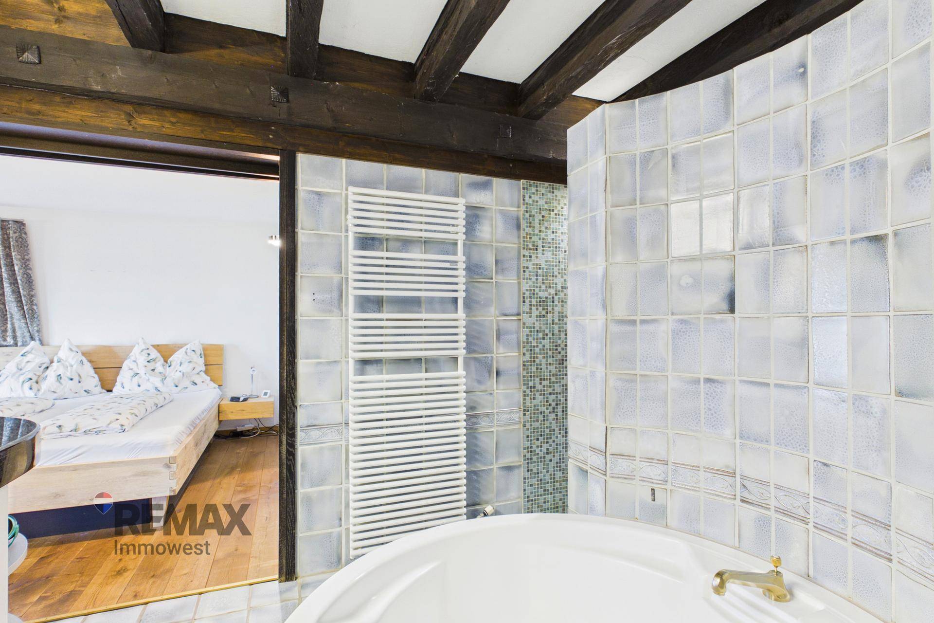 Badezimmer mit Badewanne, Handtuchheizkörper und Glasbausteinwand.