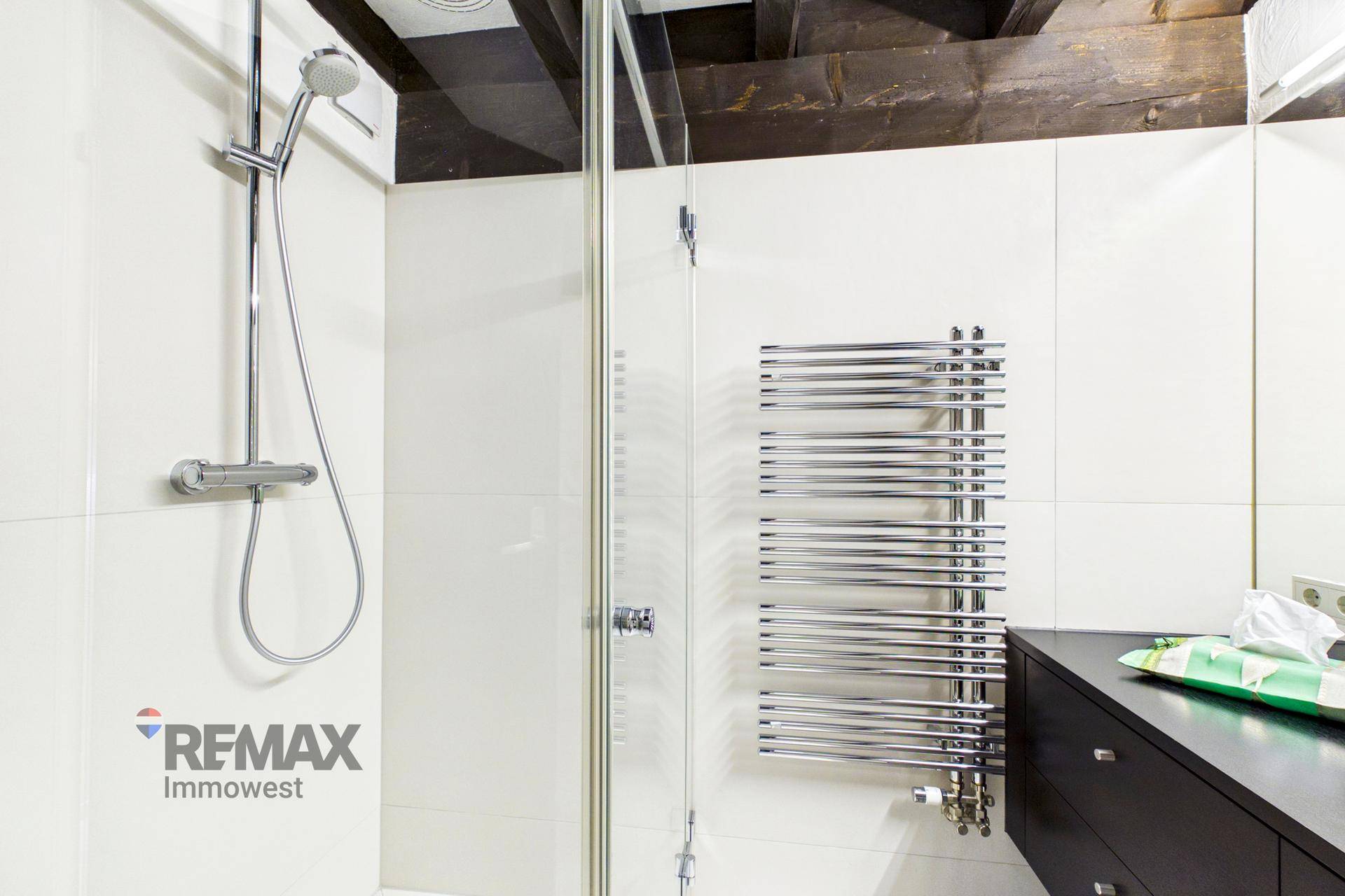 Detaillierte Ansicht der modernen Dusche mit Glasabtrennung und beheiztem Handtuchhalter.