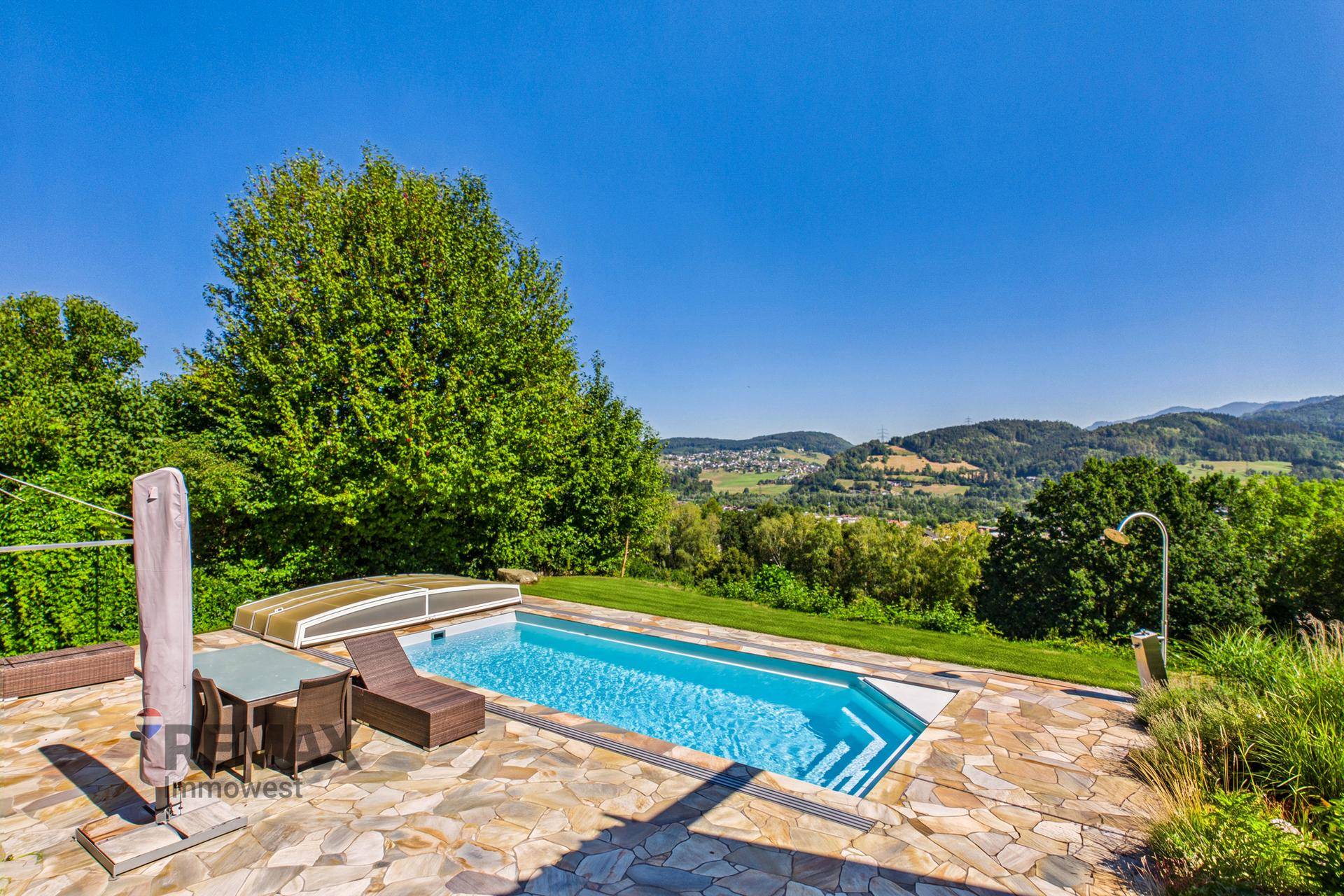 Panoramablick auf den Poolbereich mit Liegestühlen und weitreichender Aussicht auf die Landschaft.