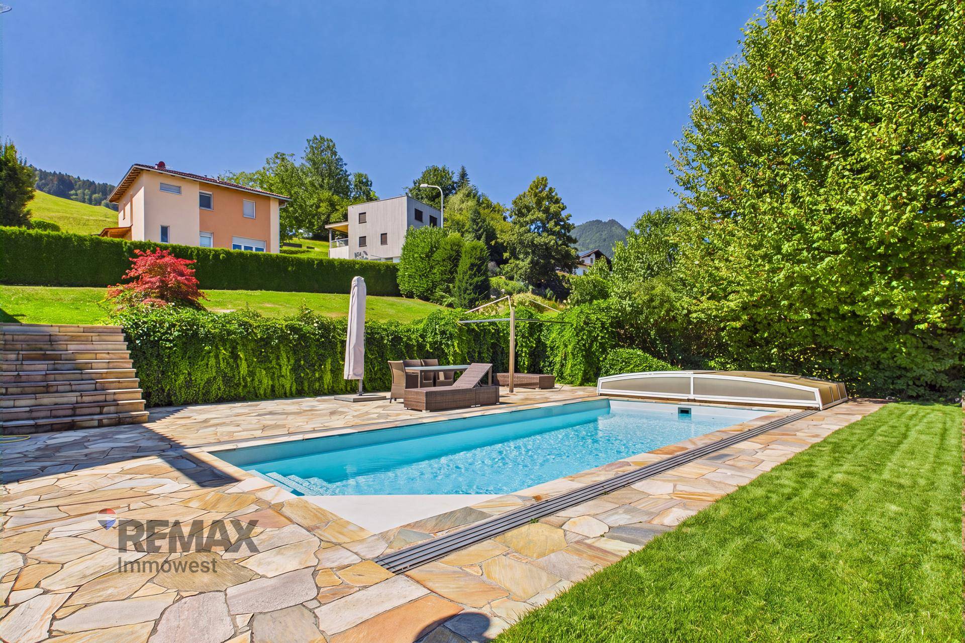 Großer Außenbereich mit Pool, Sonnenterrasse und Gartenmöbeln, umgeben von viel Grün.