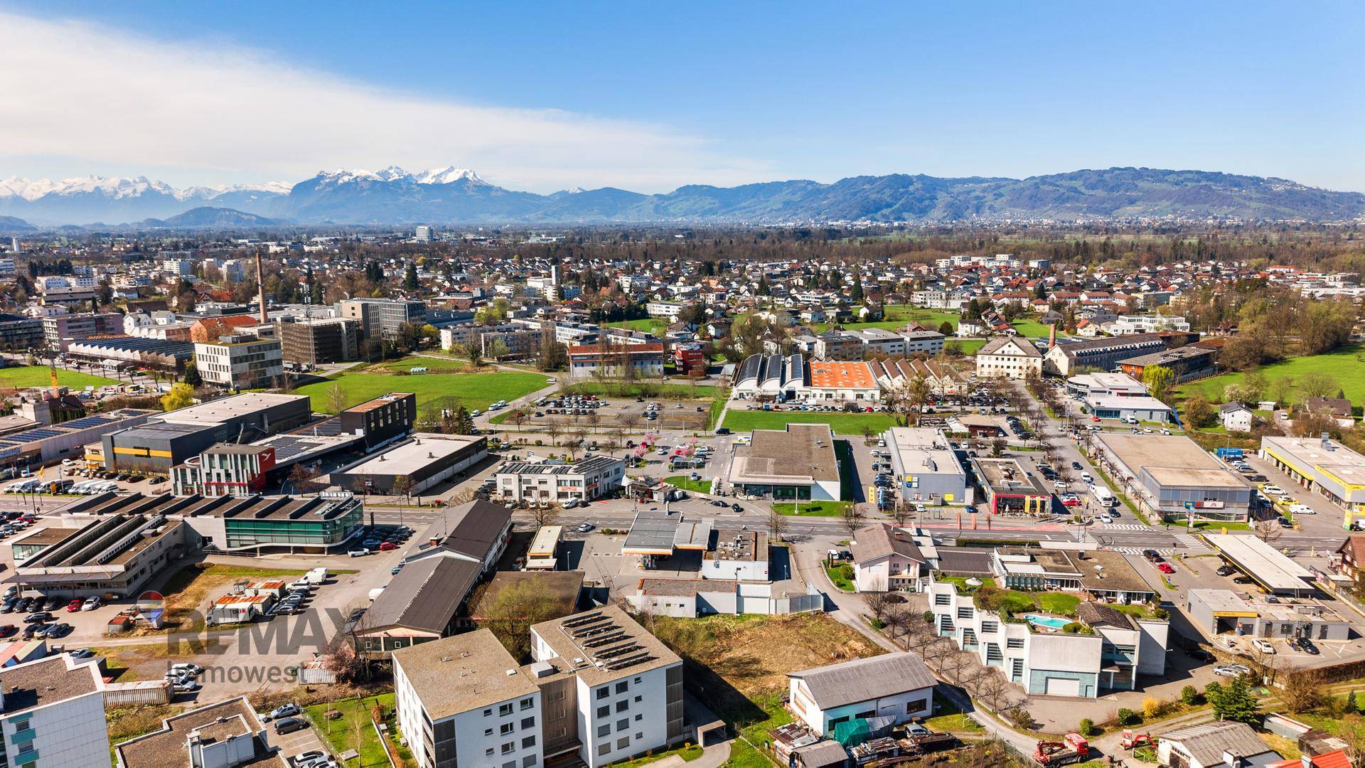 Panoramablick aus der Luft über eine Stadt mit Wohn- und Gewerbegebieten vor einer beeindruckenden Bergkulisse.
