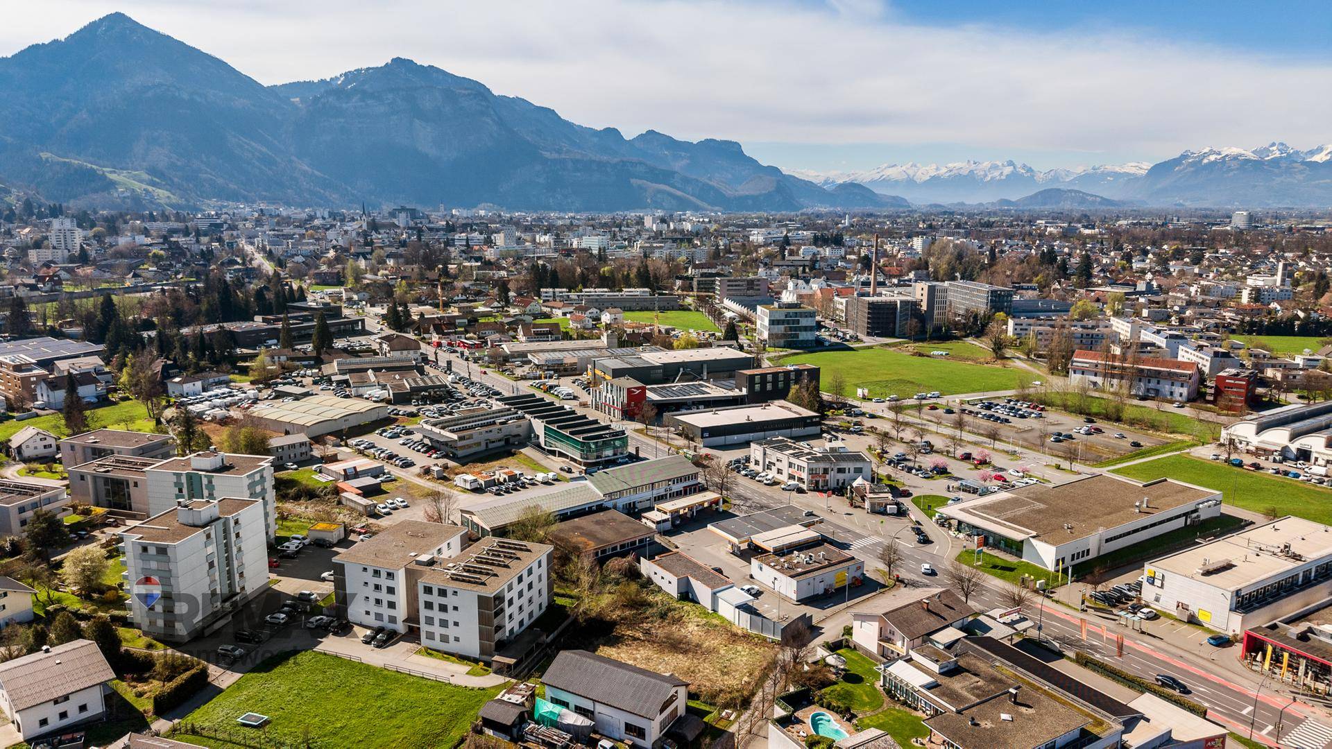 Weitläufige Luftaufnahme einer Stadtlandschaft mit Industriegebieten und schneebedeckten Bergen im Hintergrund.