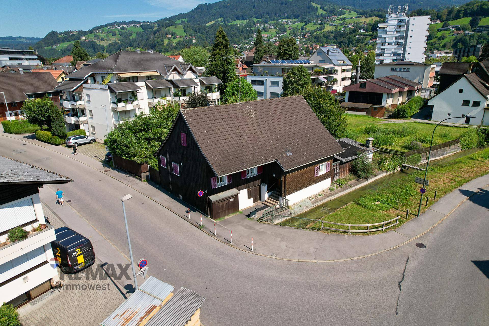 Luftaufnahme eines charmanten Holzhauses an einer Straßenecke mit Bergblick im Hintergrund.