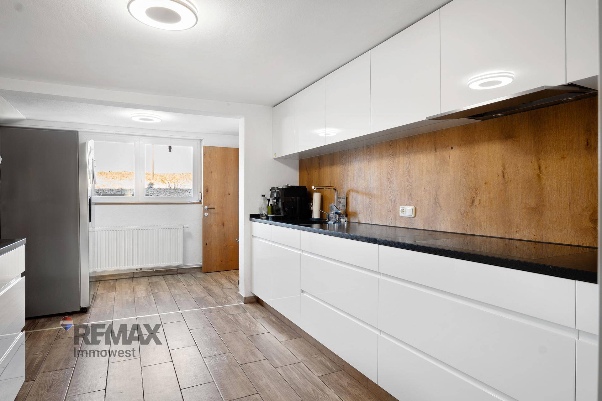 Moderne Küche mit weißen Hochglanzschränken, dunkler Arbeitsplatte und Holzrückwand.