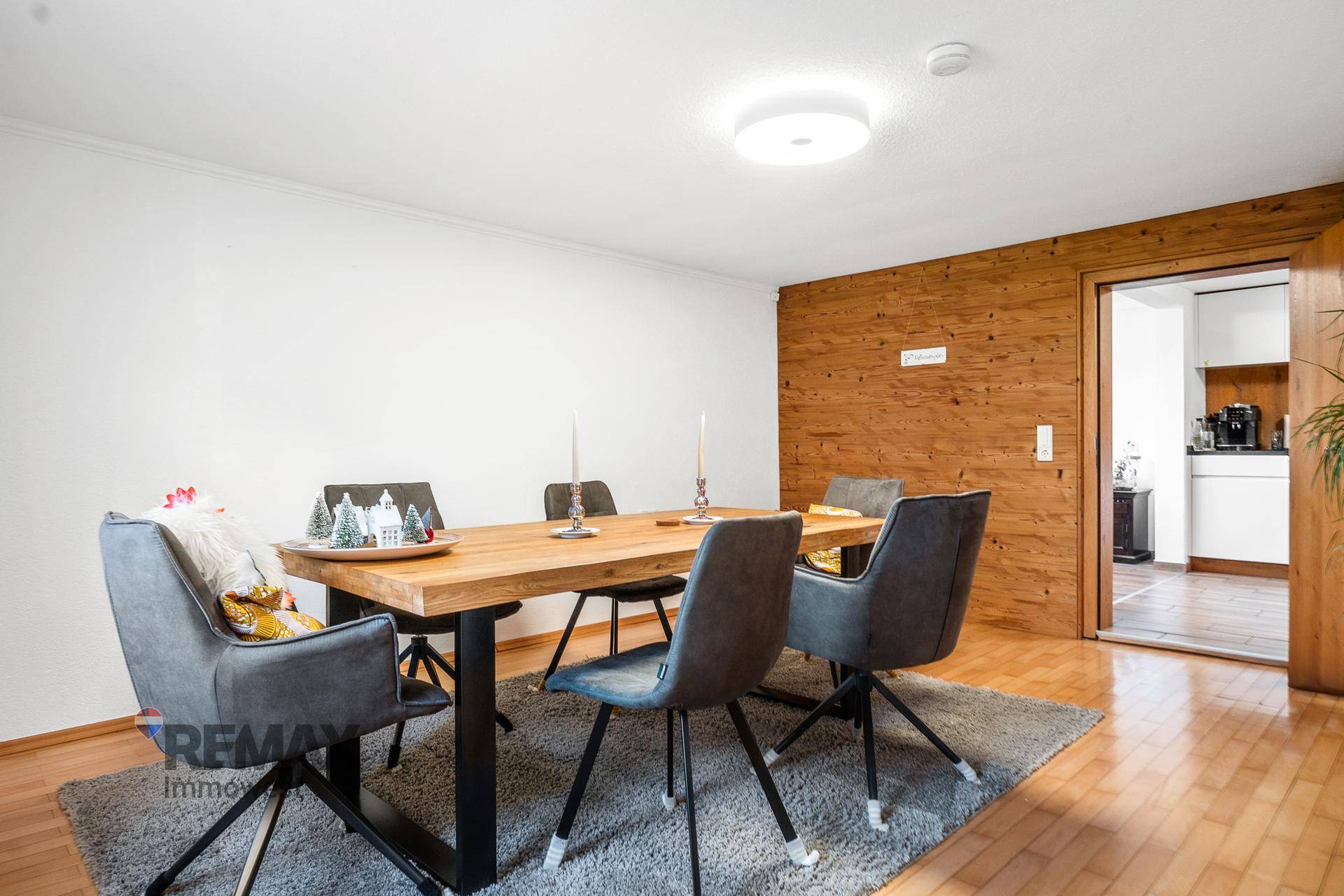 Gemütlicher Essbereich mit Holztisch, grauen Stühlen und einer Holzakzentwand, Blick zur Küche.
